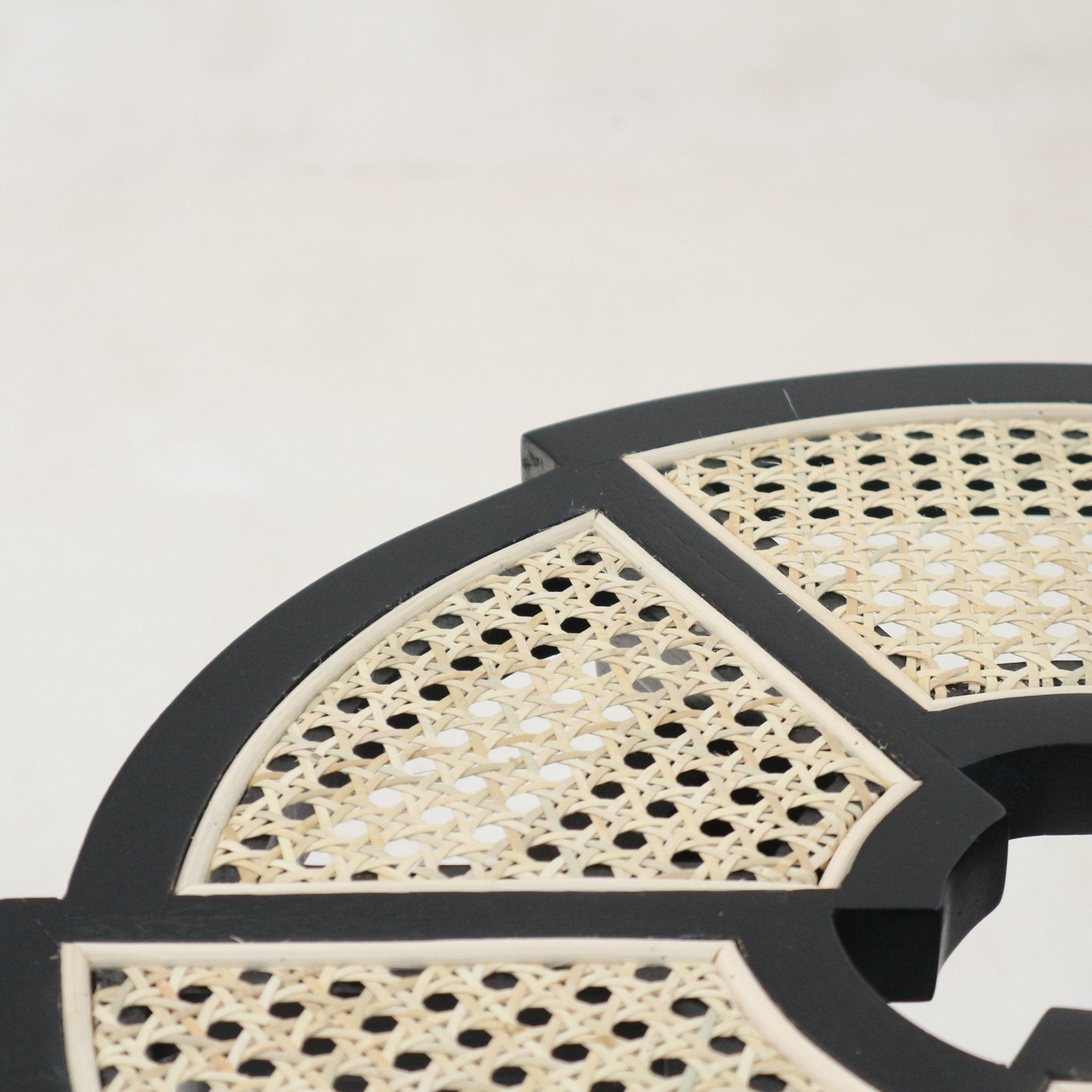 Close-up of a black-gloss wooden side table top featuring natural cream woven cane (rattan) panels set into segmented geometric frames, highlighting the cane weave and black wood trim.