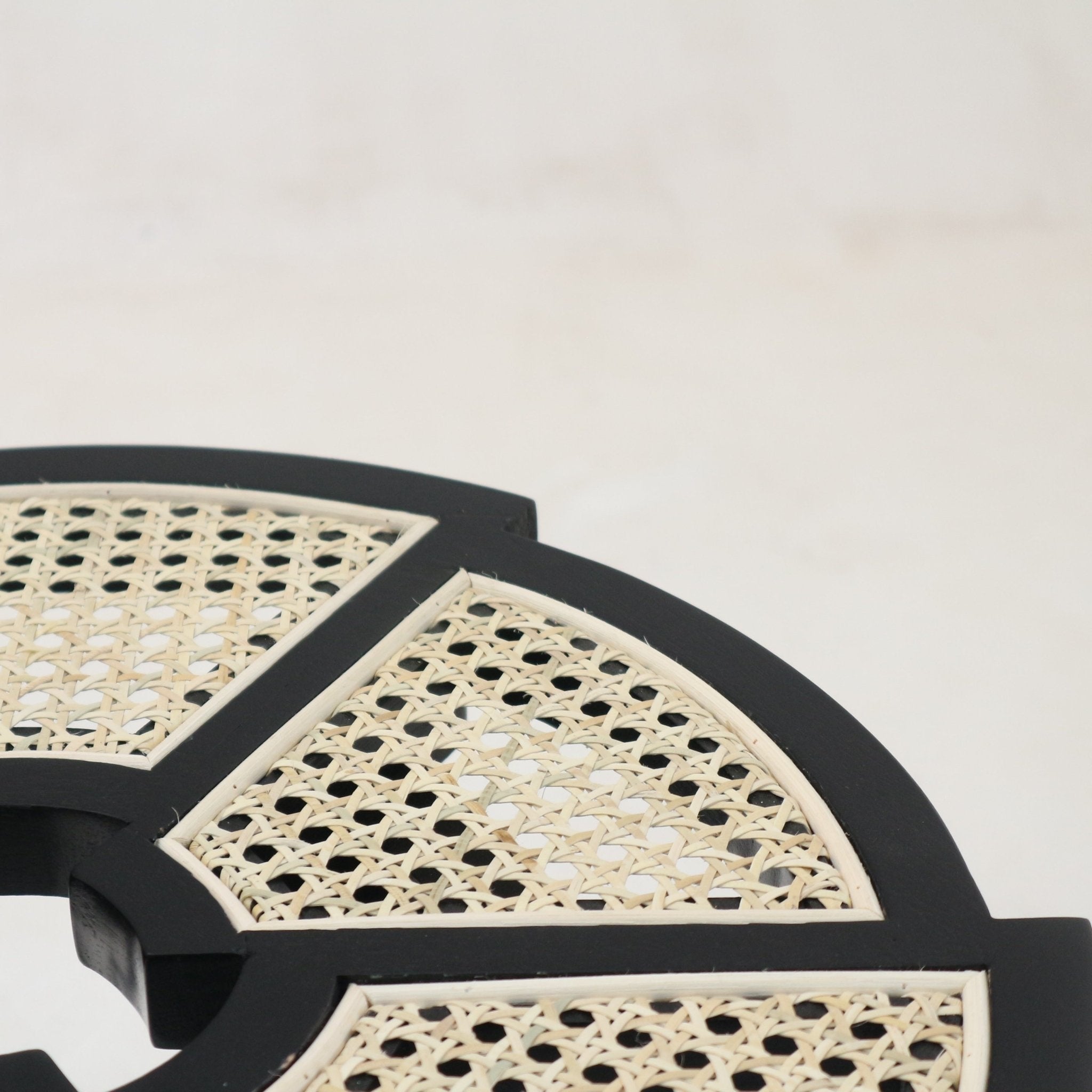 Close-up of a round side table top showing a black gloss wooden frame with natural cane rattan panels arranged in segmented geometric sections.