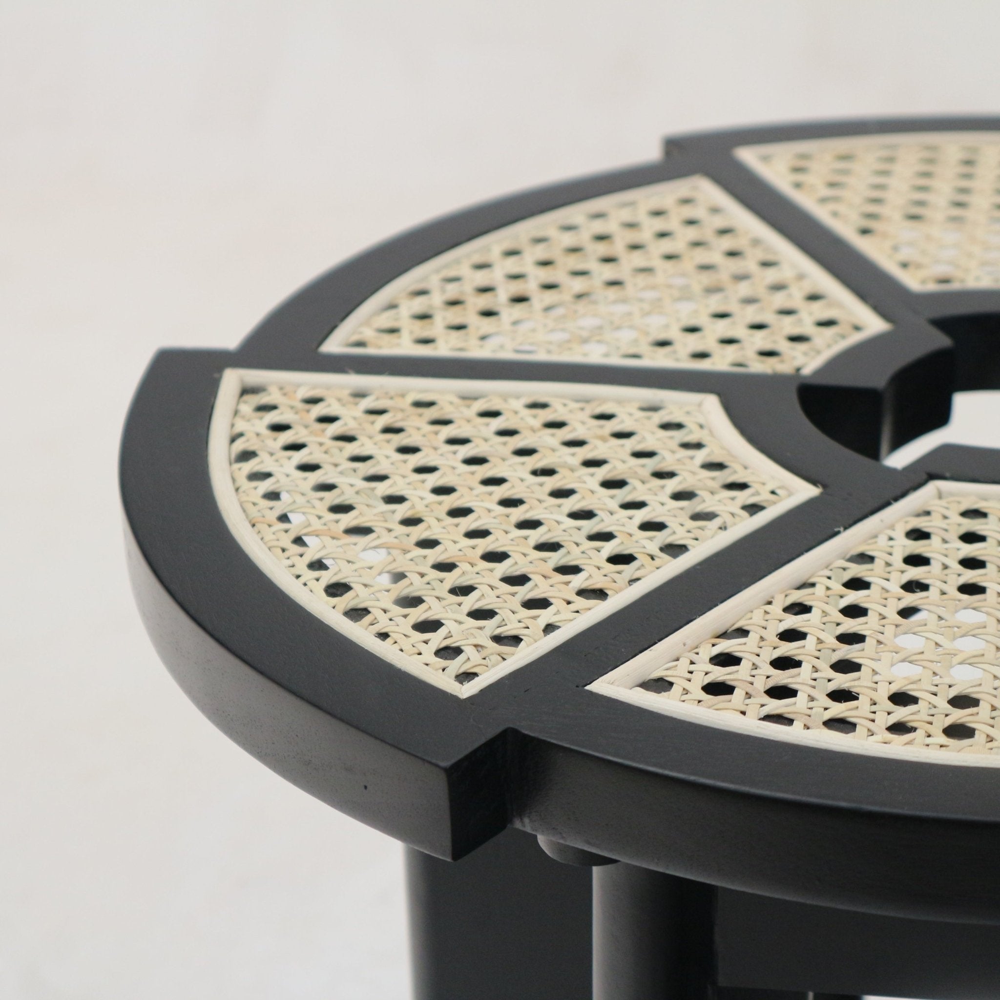 Close-up of a round side table top showing a black gloss solid wood frame with segmented natural cane rattan insets and a subtle notch detail along the edge.