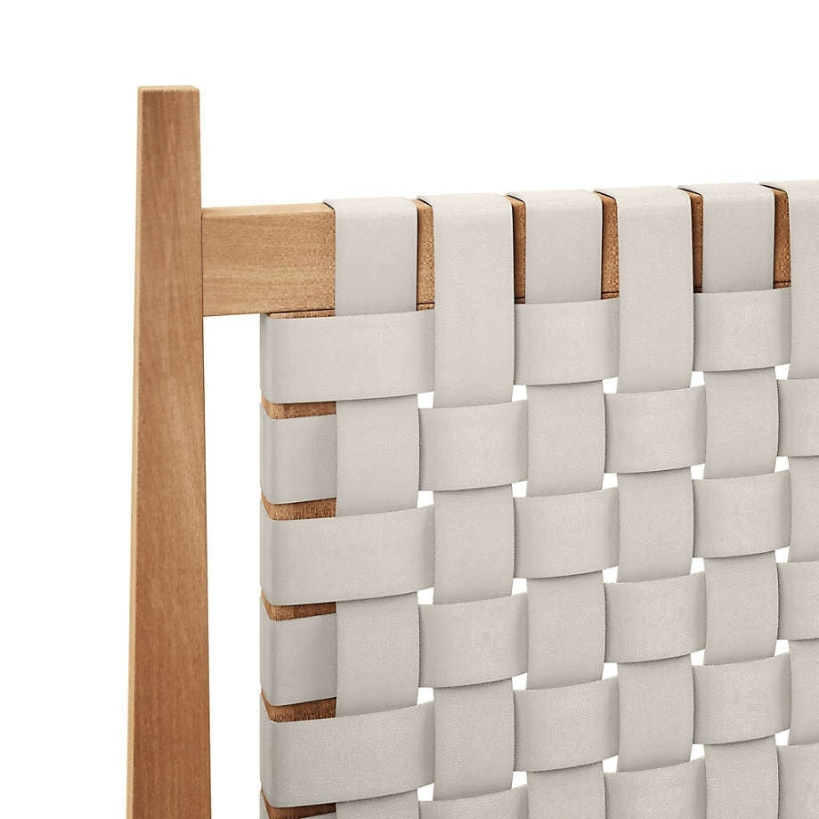Close-up of a teak bed headboard with wide cream faux-leather straps woven in a basket pattern over a natural wood frame.