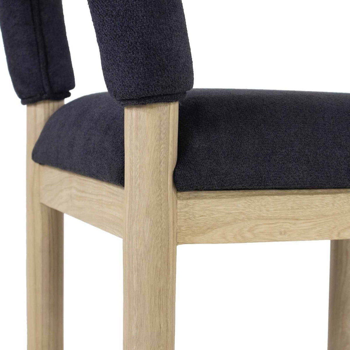 Close-up of a charcoal bouclé upholstered seat and low back on a light oak stool frame, highlighting the textured fabric and natural oak grain.