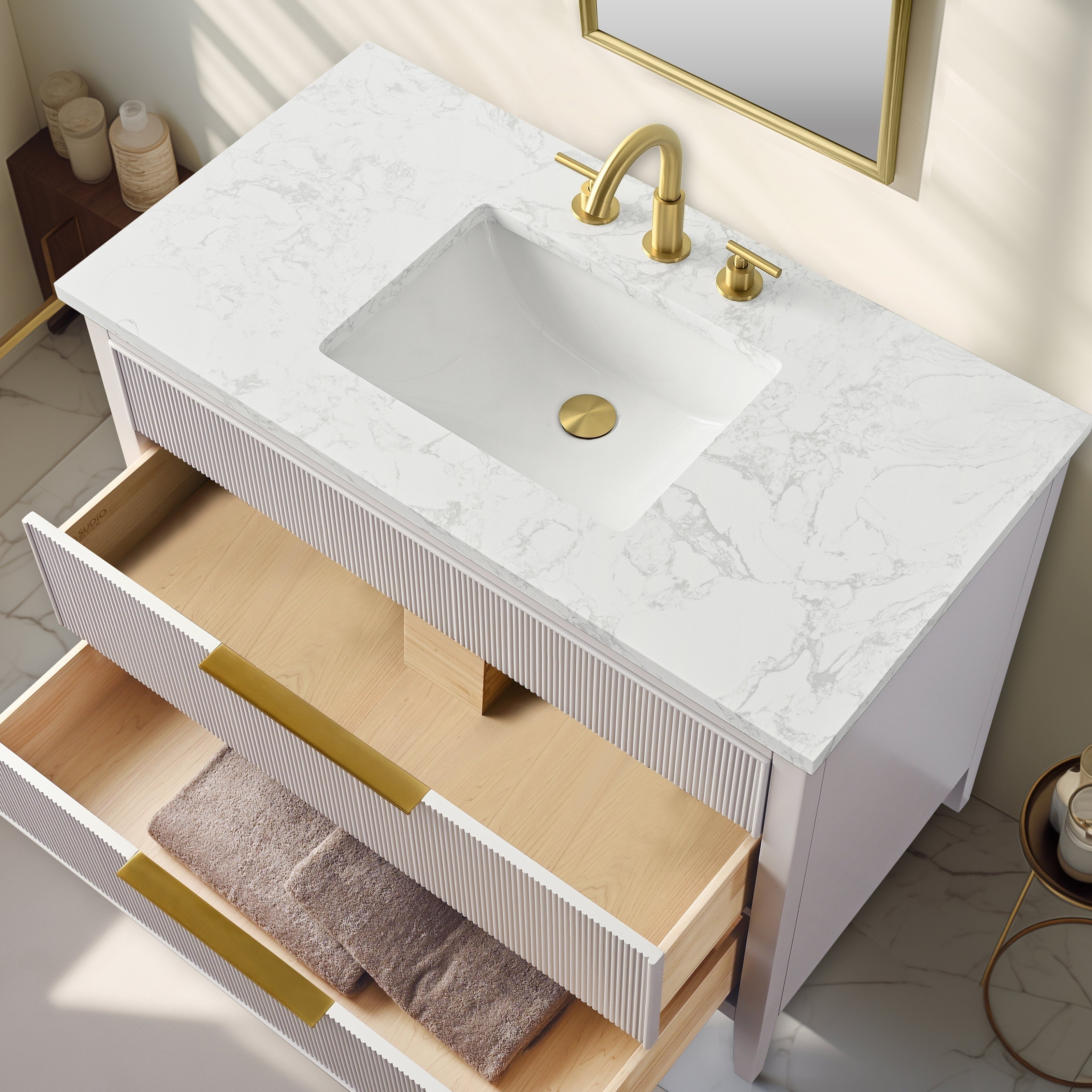 Top-down view of a modern single-sink bathroom vanity with veined white stone top, rectangular integrated ceramic sink, brass-finish faucet and drain, white fluted wood drawer fronts with gold bar pulls and natural wood interiors.
