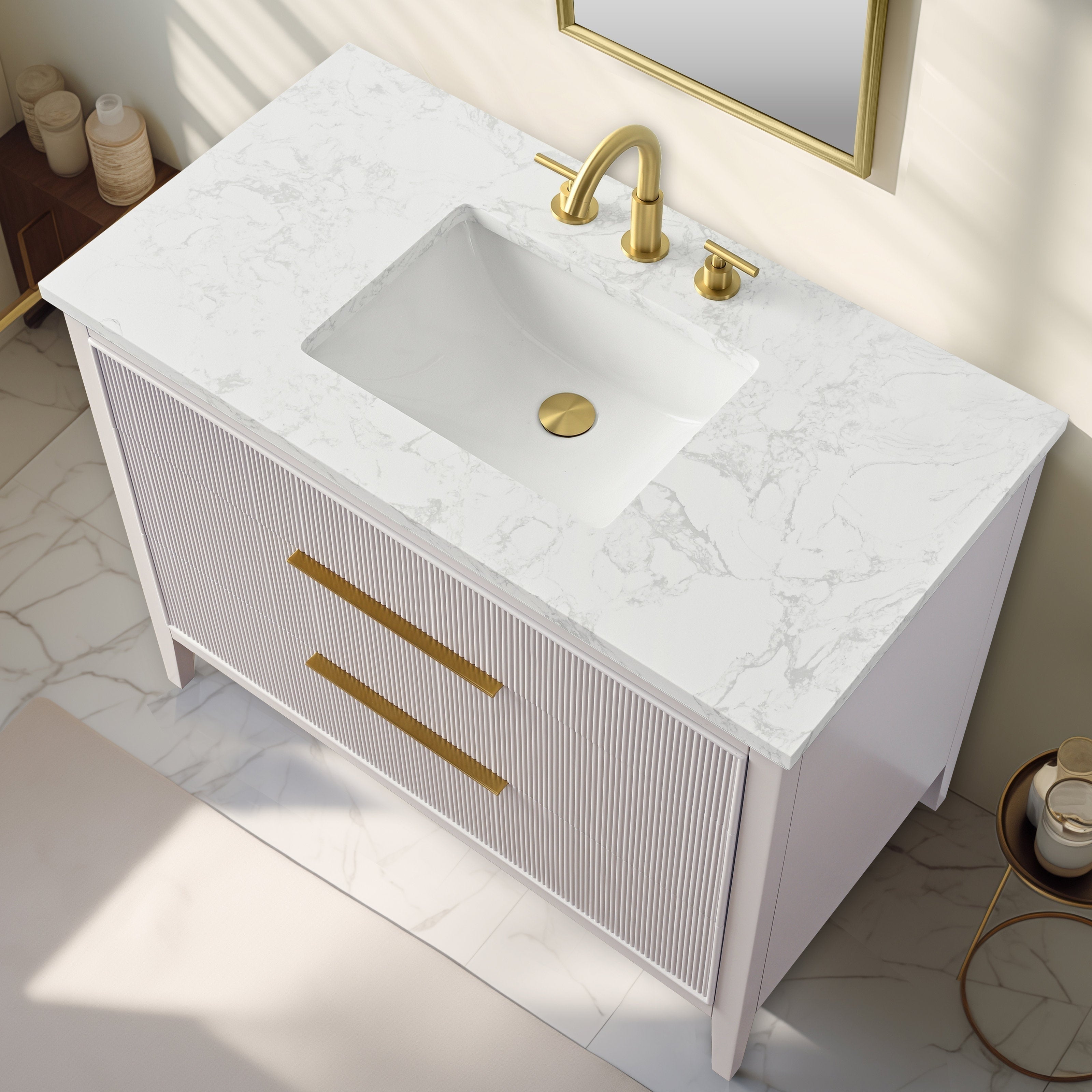 Top-down view of a modern single-sink bathroom vanity with white marbled stone top and integrated rectangular white sink, fluted light-stone solid wood cabinet, long gold drawer pulls and matching gold faucet and drain.