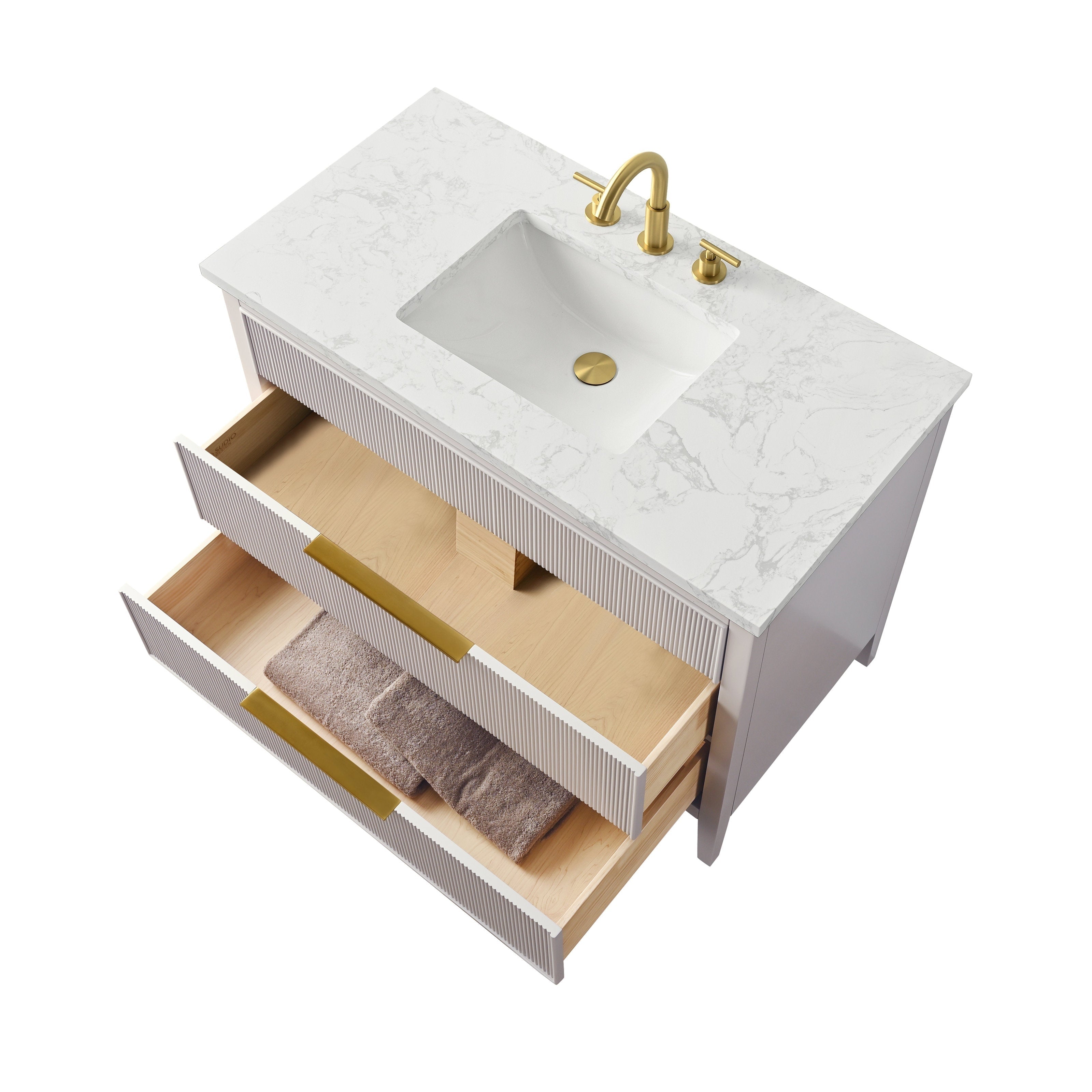 Modern freestanding single-sink bathroom vanity with a white stone top and undermount rectangular sink, brass faucet and drain, fluted solid wood white cabinet with two open drawers showing light wood interiors and folded brown towels.