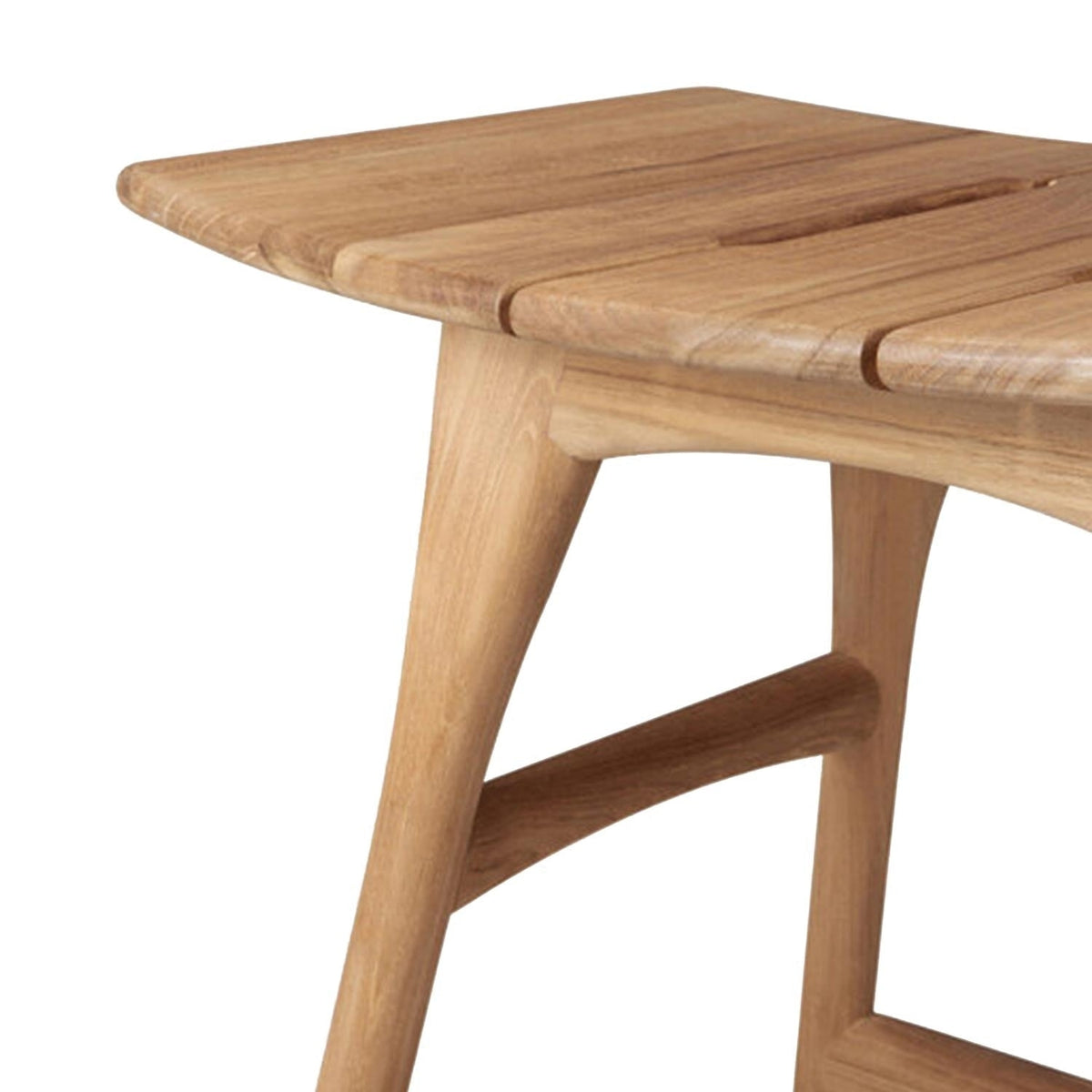 Close-up of a natural teak backless shower stool showing the slatted seat corner, rounded edge, tapered leg and curved stretcher in a contemporary coastal style.