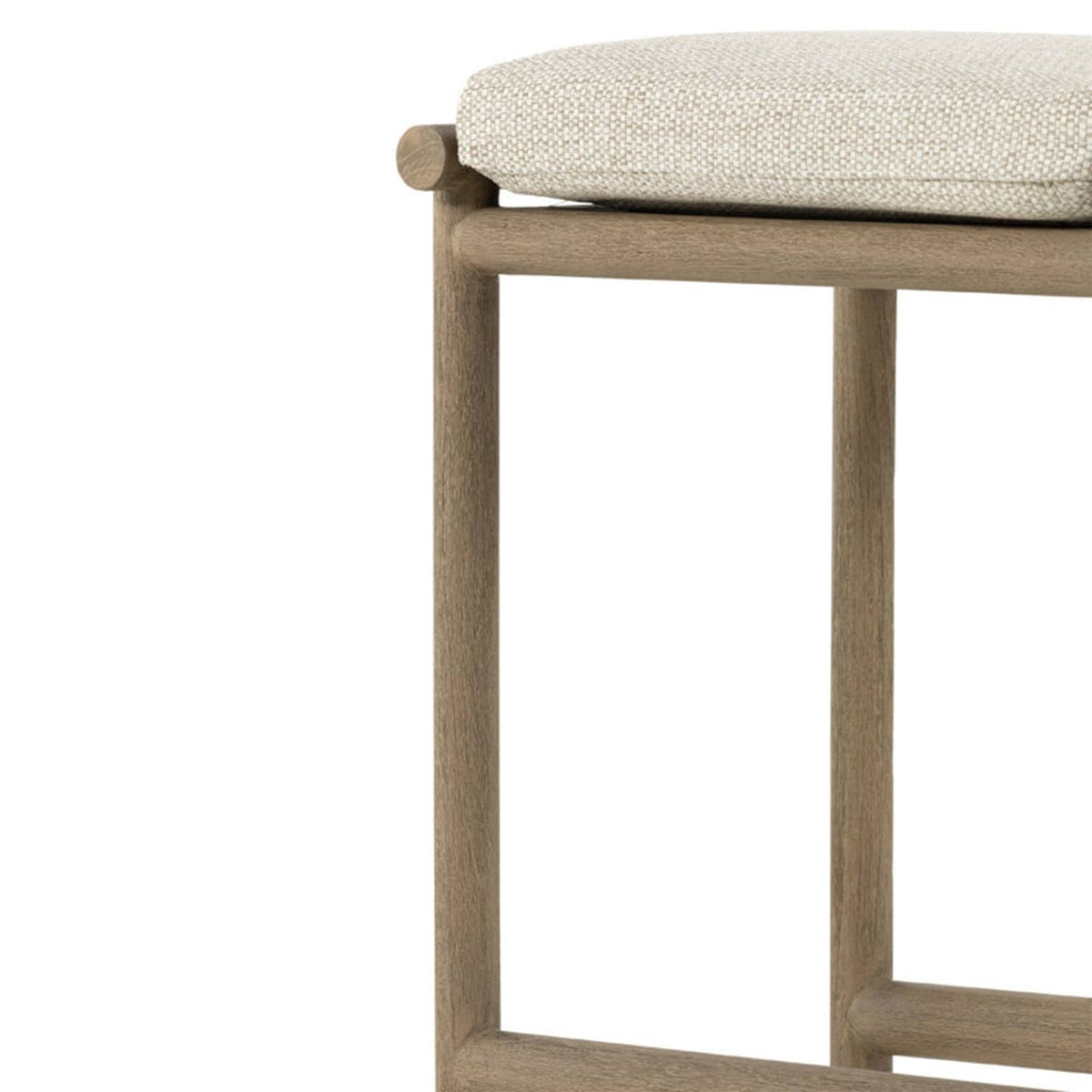 Close-up of a teak wood bar stool frame with squared legs and horizontal stretchers supporting a beige textured upholstered backless seat cushion in a coastal-contemporary outdoor style.