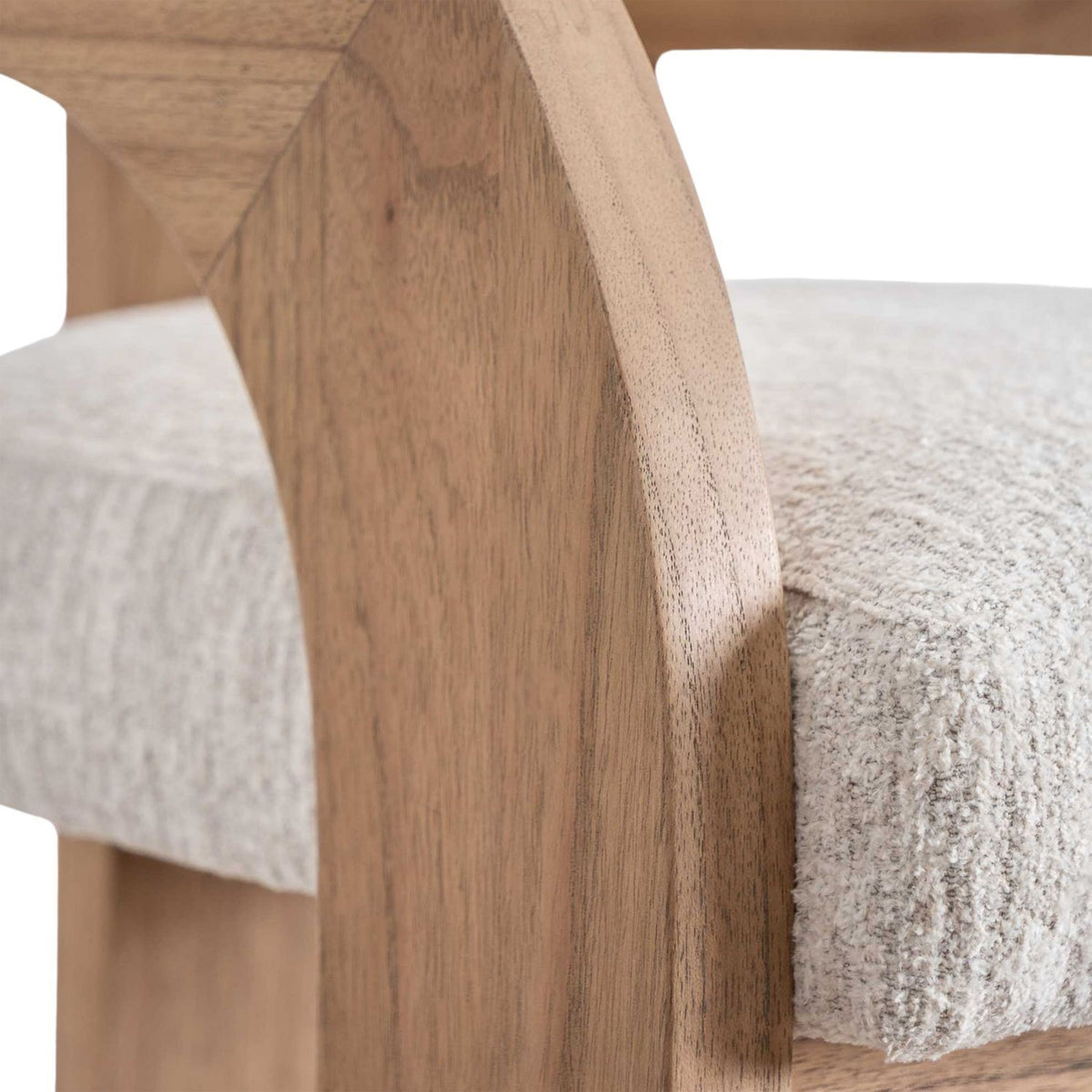 Close-up of the stool’s natural wood U-shaped arm and back next to the textured cream fabric upholstered seat.