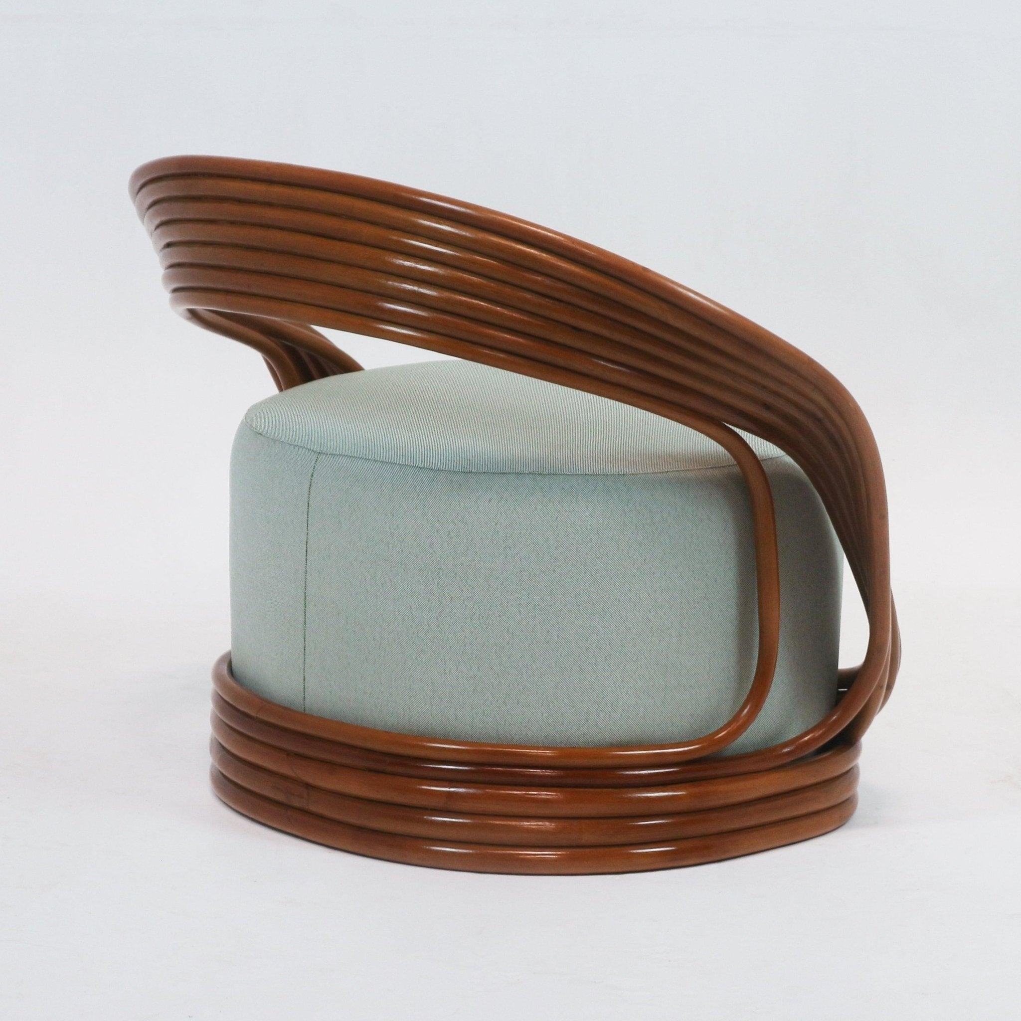 Side view of a mid-century modern lounge chair with a rounded pale green fabric cushion embraced by a layered brown cane rattan frame forming a continuous curved back and circular base.