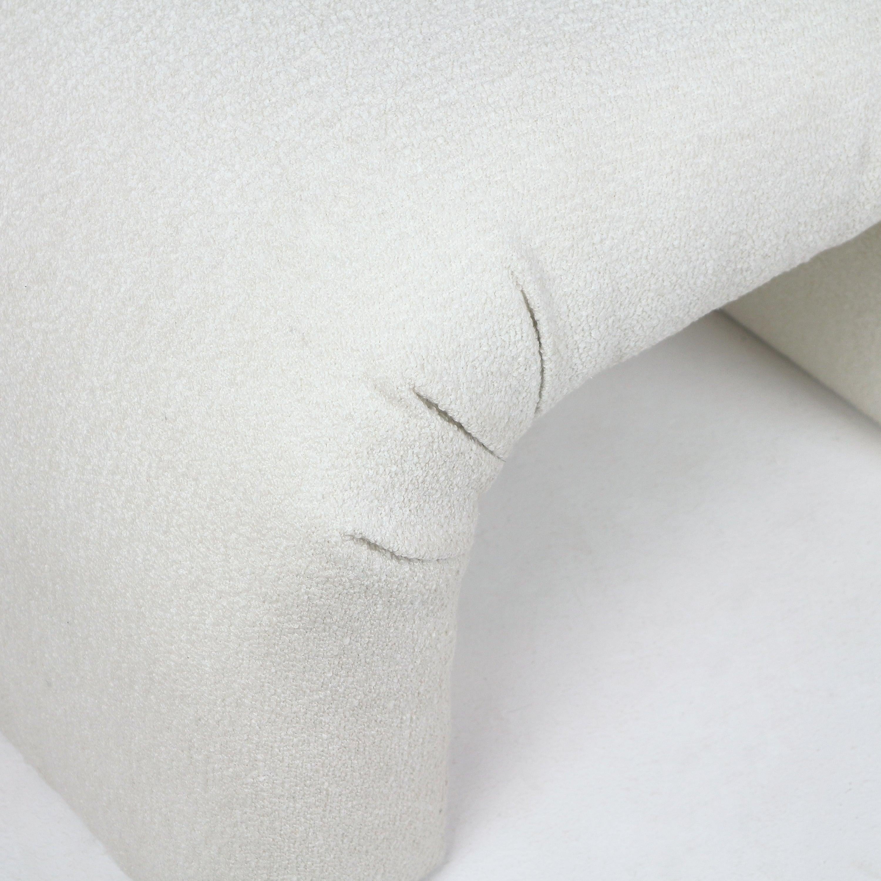 Close-up of a cream boucle upholstered vanity bench corner showing the curved arch detail, looped textured fabric and visible stitched seams.
