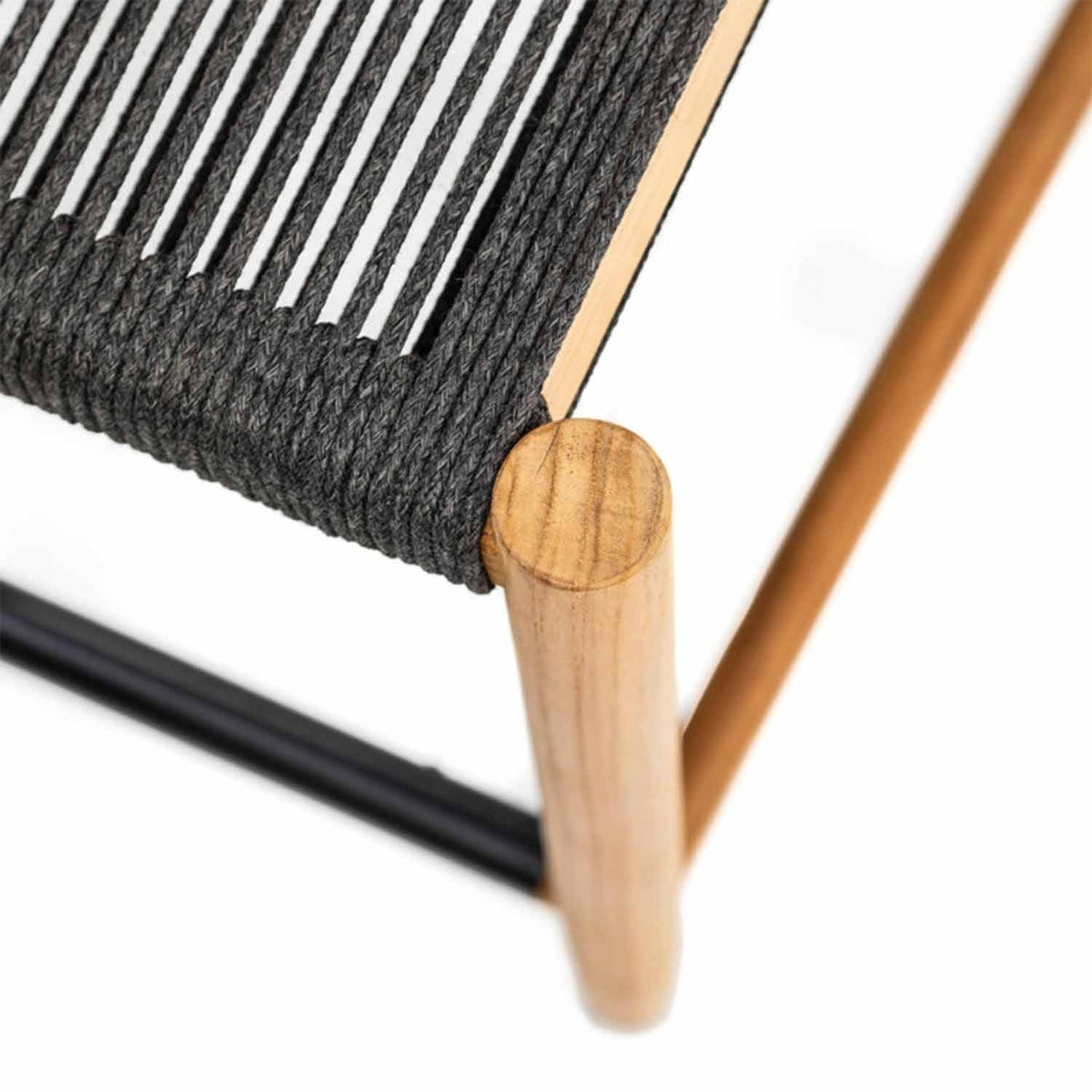 Close-up of a teak outdoor bar stool corner showing a natural teak rounded leg, gray woven cord seat wrapped around the frame and a black metal footrest.