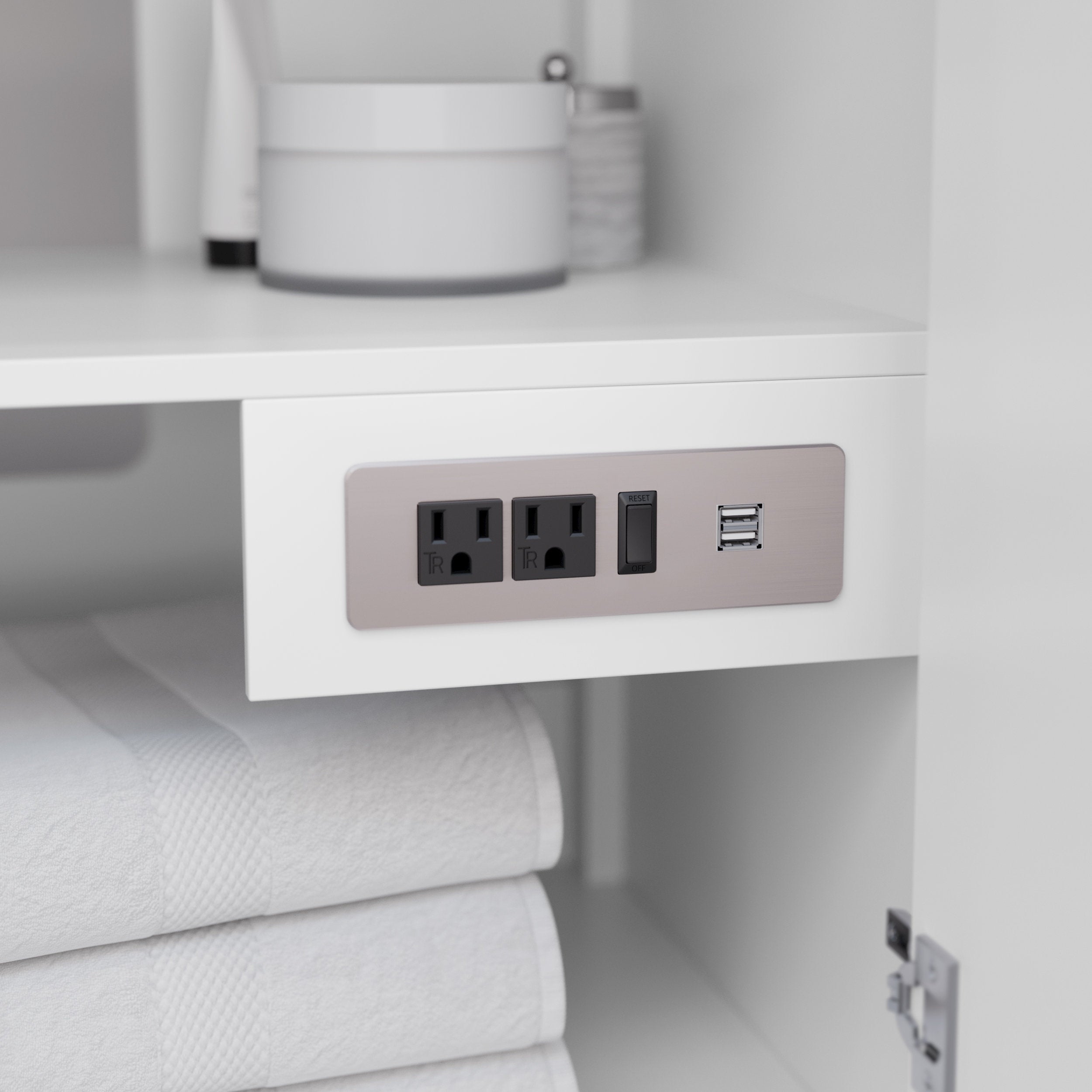 Close-up of a modern white wooden vanity interior showing a built-in brushed-stone outlet panel with two black electrical sockets, a reset/GFCI switch and dual USB ports; folded white towels sit on the shelf below.