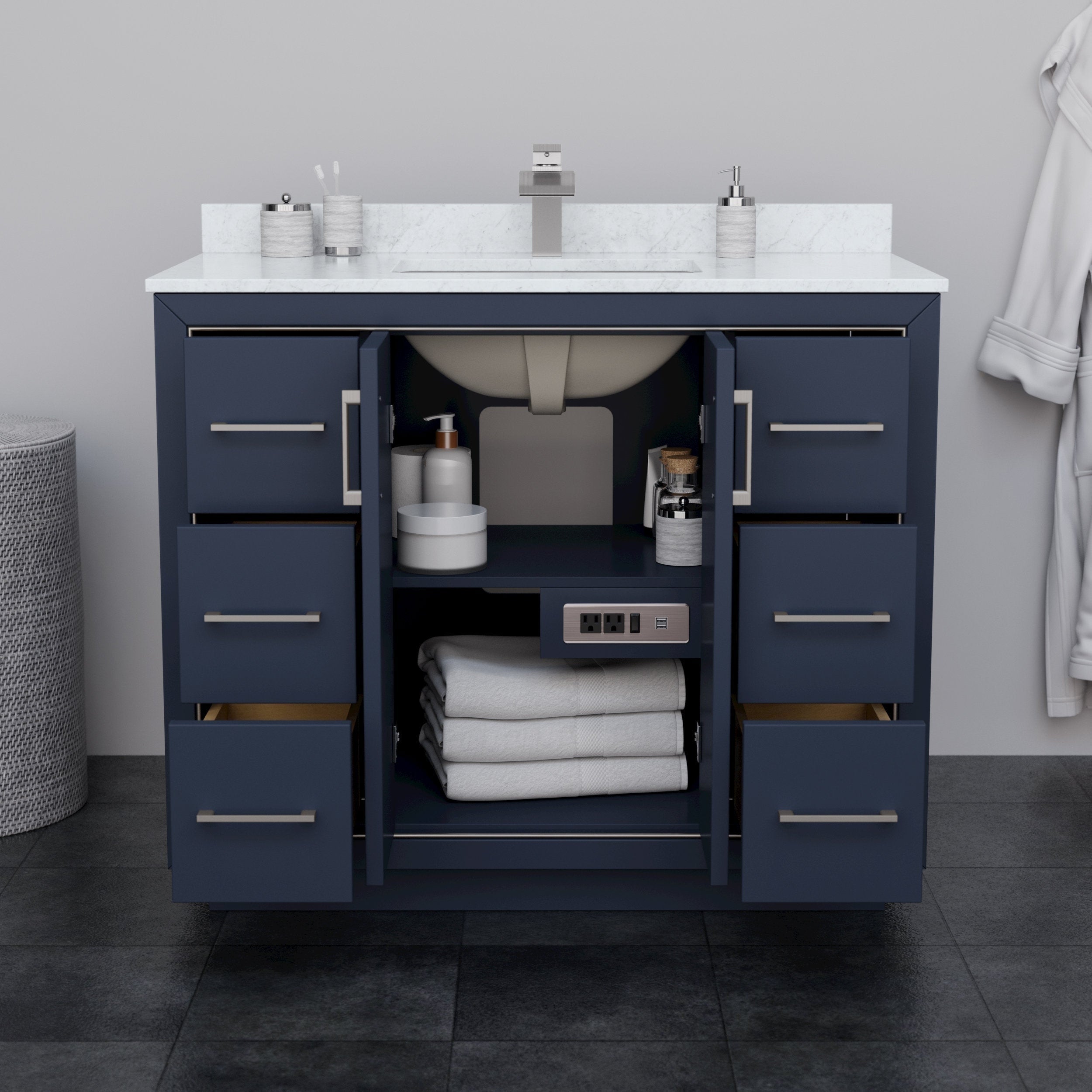 Modern 42-inch solid wood bathroom vanity in navy blue with a white stone countertop and undermount ceramic sink, brushed-nickel pulls, open center doors showing shelves with folded towels, toiletries and a built-in power outlet.