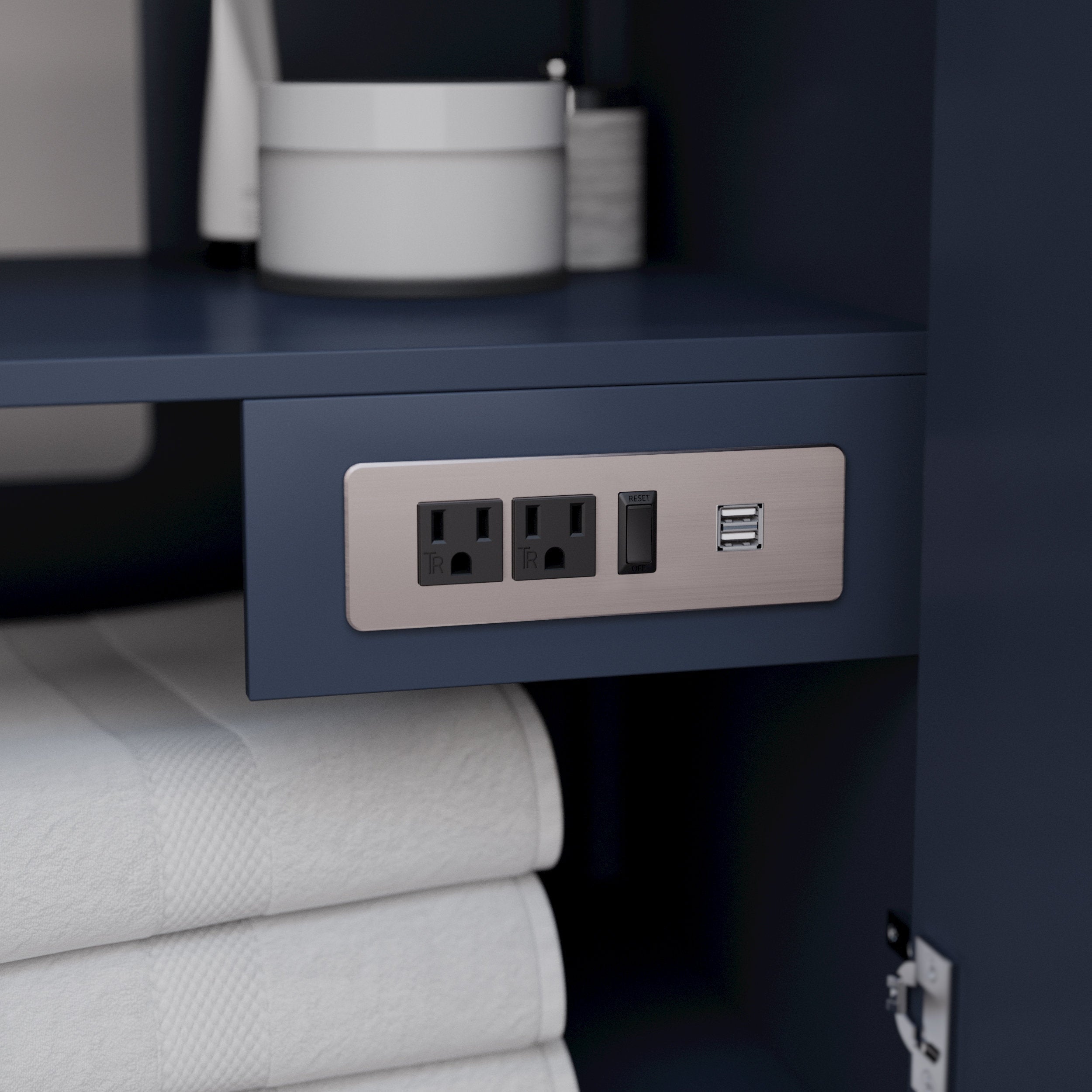 Close-up of a stone-finish solid wood vanity interior showing a brushed-nickel power plate with two grounded outlets, a reset switch and dual USB ports mounted under a shelf above neatly folded white towels.