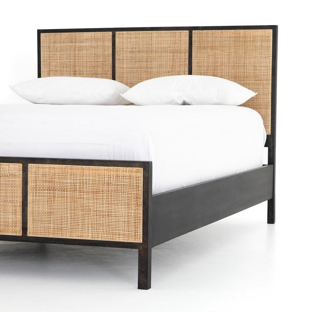 Angled view of a boho teak bed with dark solid wood frame and woven rattan cane panels on the headboard and footboard, styled with white bedding.