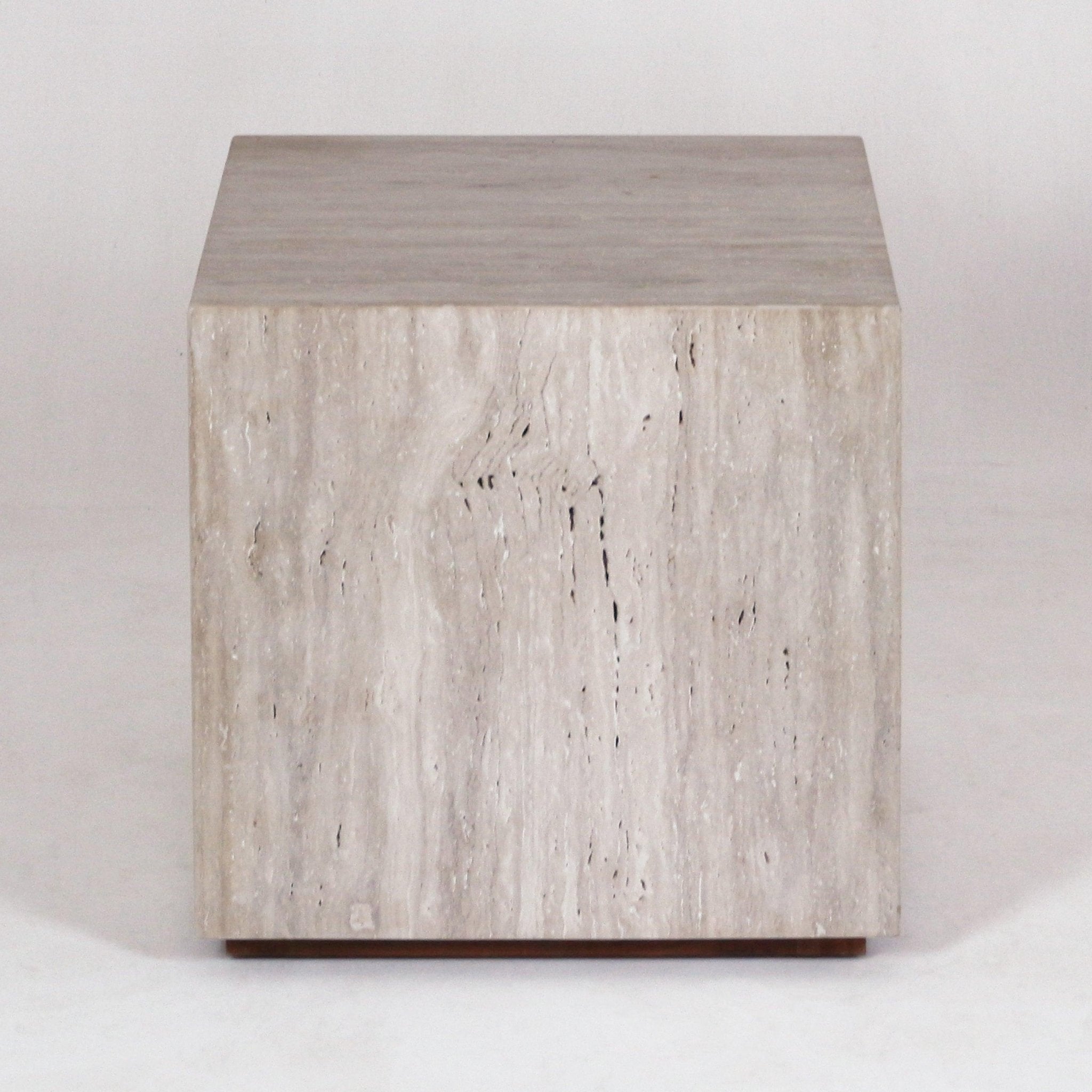 Front-facing view of a modern cube-shaped nightstand carved from natural travertine marble with neutral beige stone veining and a low wooden plinth base.