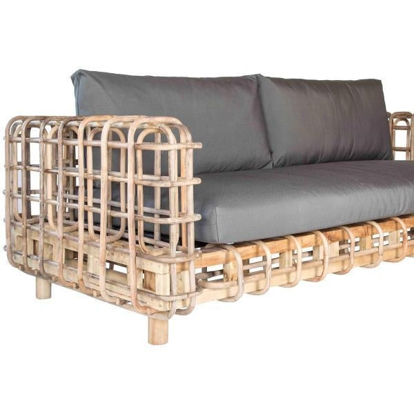 Natural rattan-framed boho sofa with open woven grid arms and base, fitted with thick gray fabric seat and back cushions.