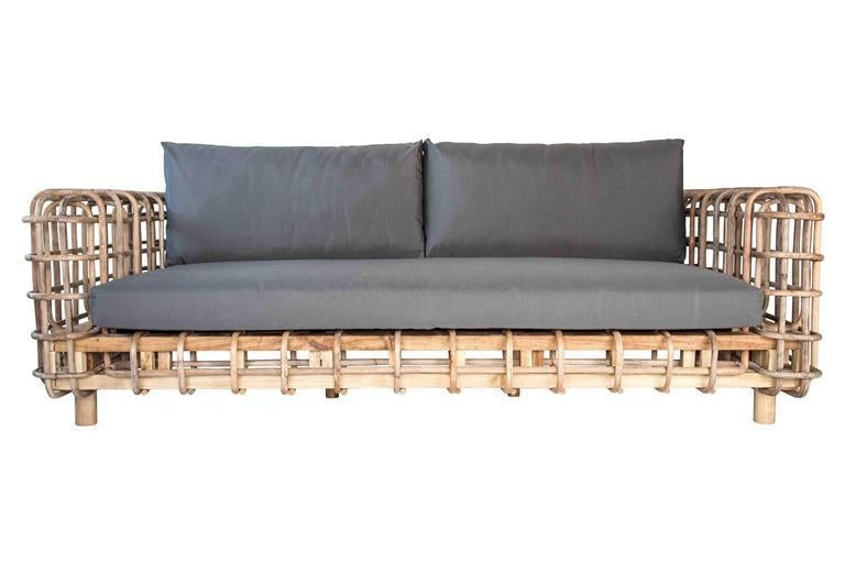 Boho-style sofa with a natural rattan woven frame and low legs, topped with a grey fabric seat cushion and two matching grey back cushions on a white background.