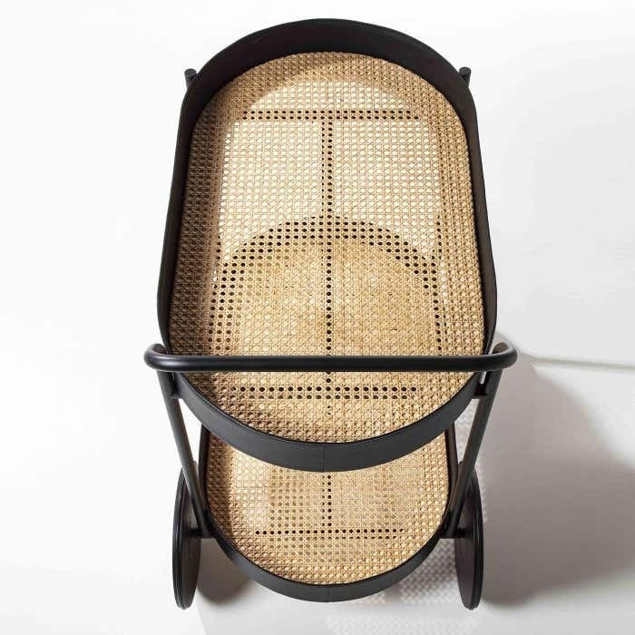 Top-down view of a modern matte black metal two-tier bar cart with woven natural rattan cane shelves and oversized black wheels.