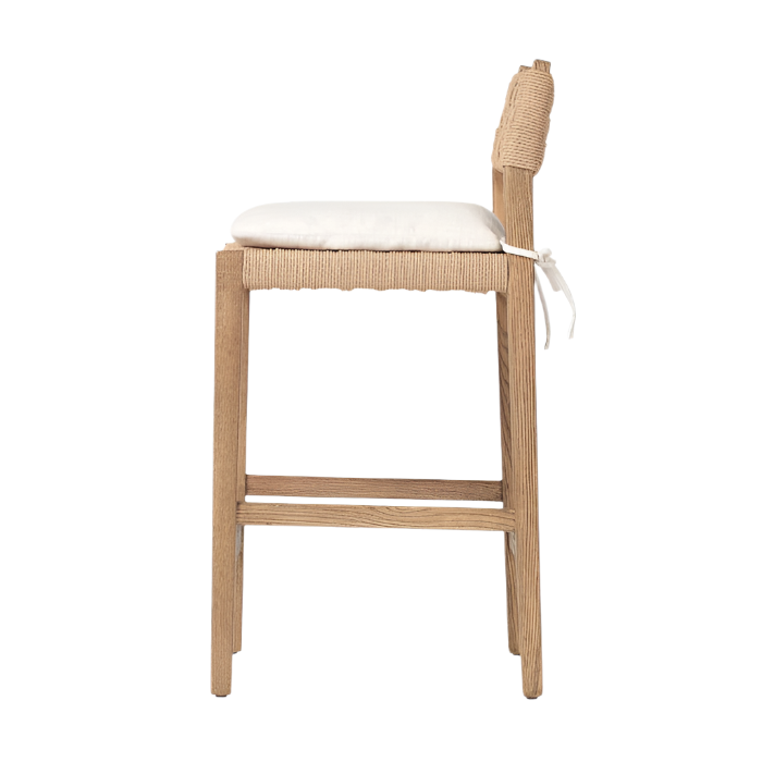 Side view of a modern counter stool with a natural oak frame, woven papercord back and seat apron, a white tied seat cushion, and a horizontal footrest.