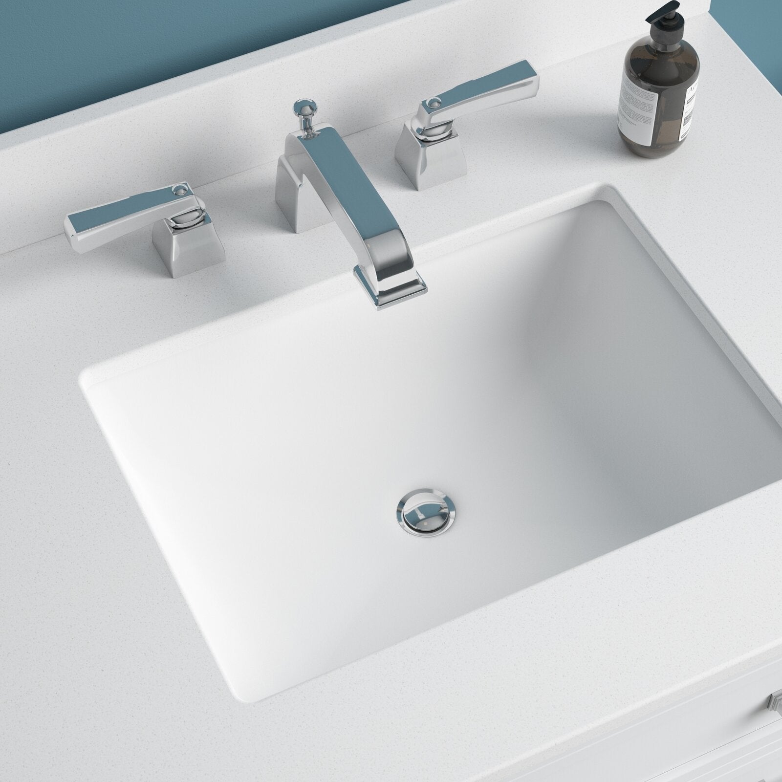 Top-down view of a modern stone-colored vanity top with a white rectangular undermount sink, chrome widespread faucet with lever handles, and a brown pump soap bottle on the countertop.