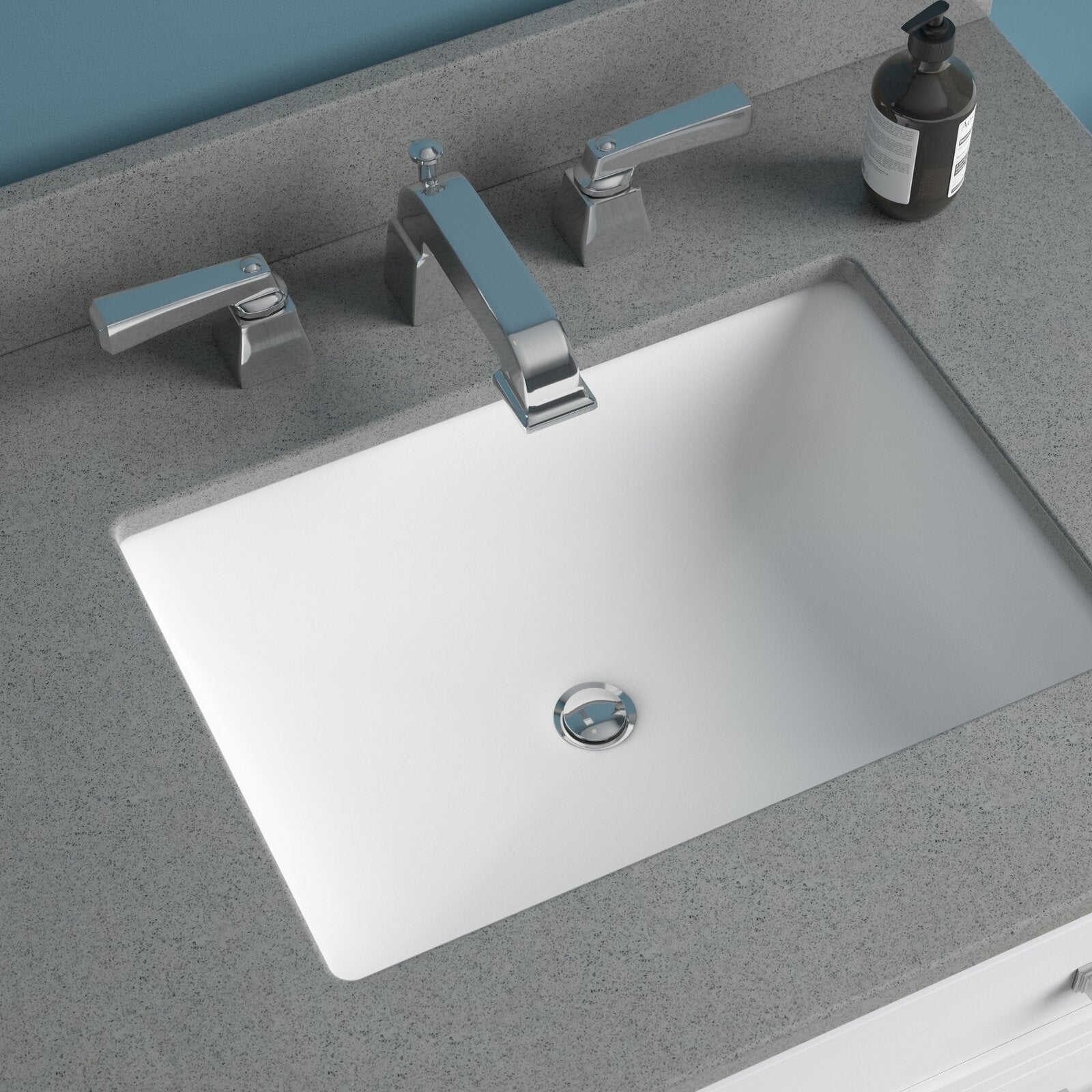 Top-down view of a white rectangular ceramic undermount sink set into a speckled stone-colored countertop with a modern chrome widespread faucet, separate lever handles and a dark soap dispenser at the back.