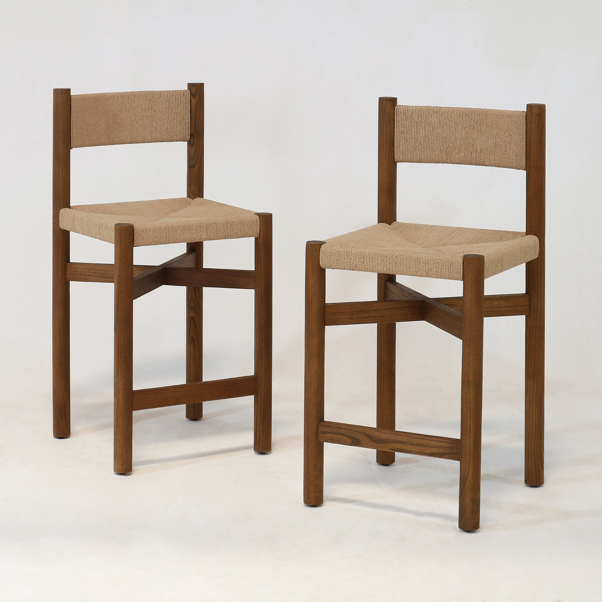 Two walnut-brown solid wood counter stools with woven natural papercord seat and back, armless square-leg frames with cross stretchers shown on a plain white background.