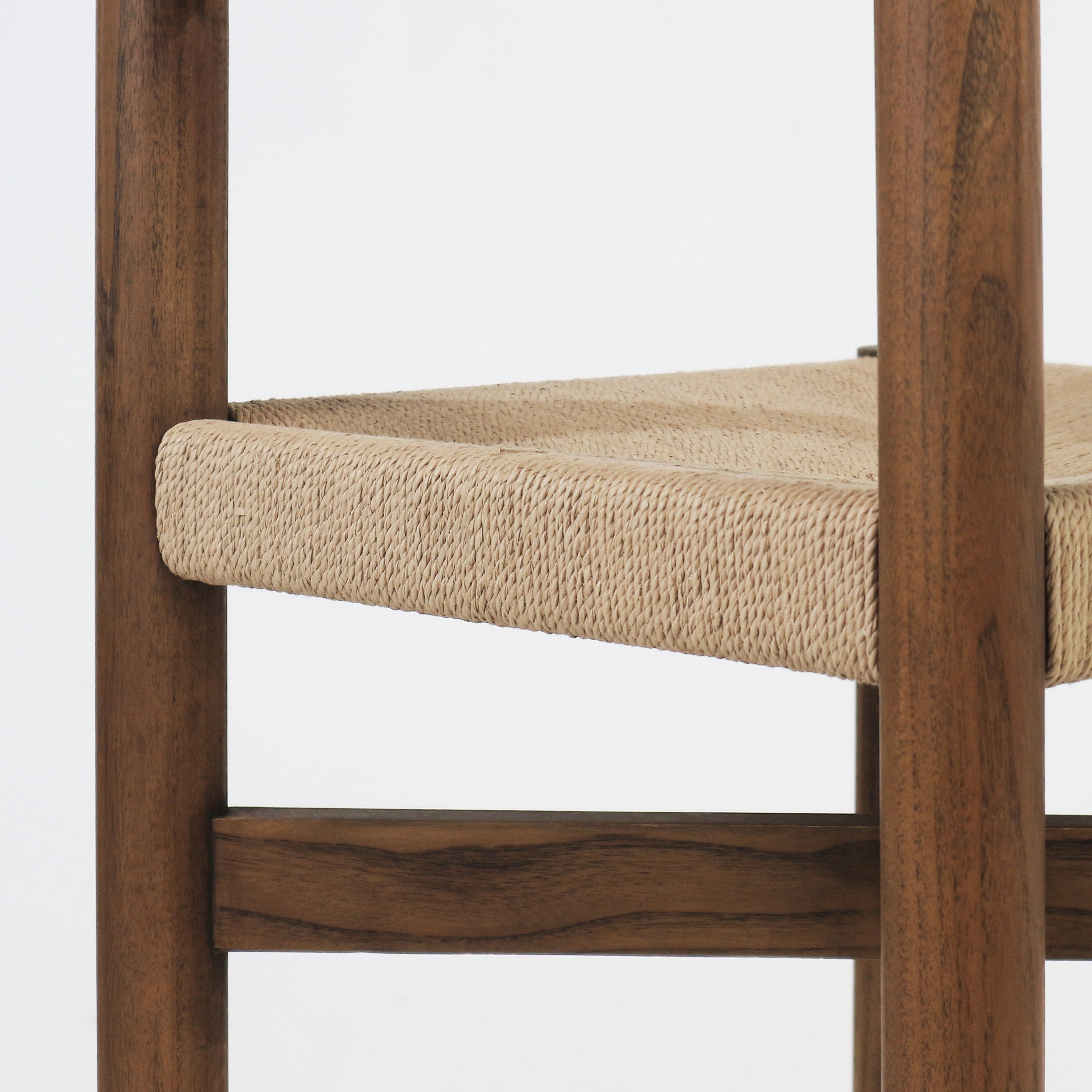 Close-up of a rush-woven natural papercord seat on a walnut-brown solid wood stool frame, showing the textured woven seat and adjacent wood leg with horizontal footrest detail.