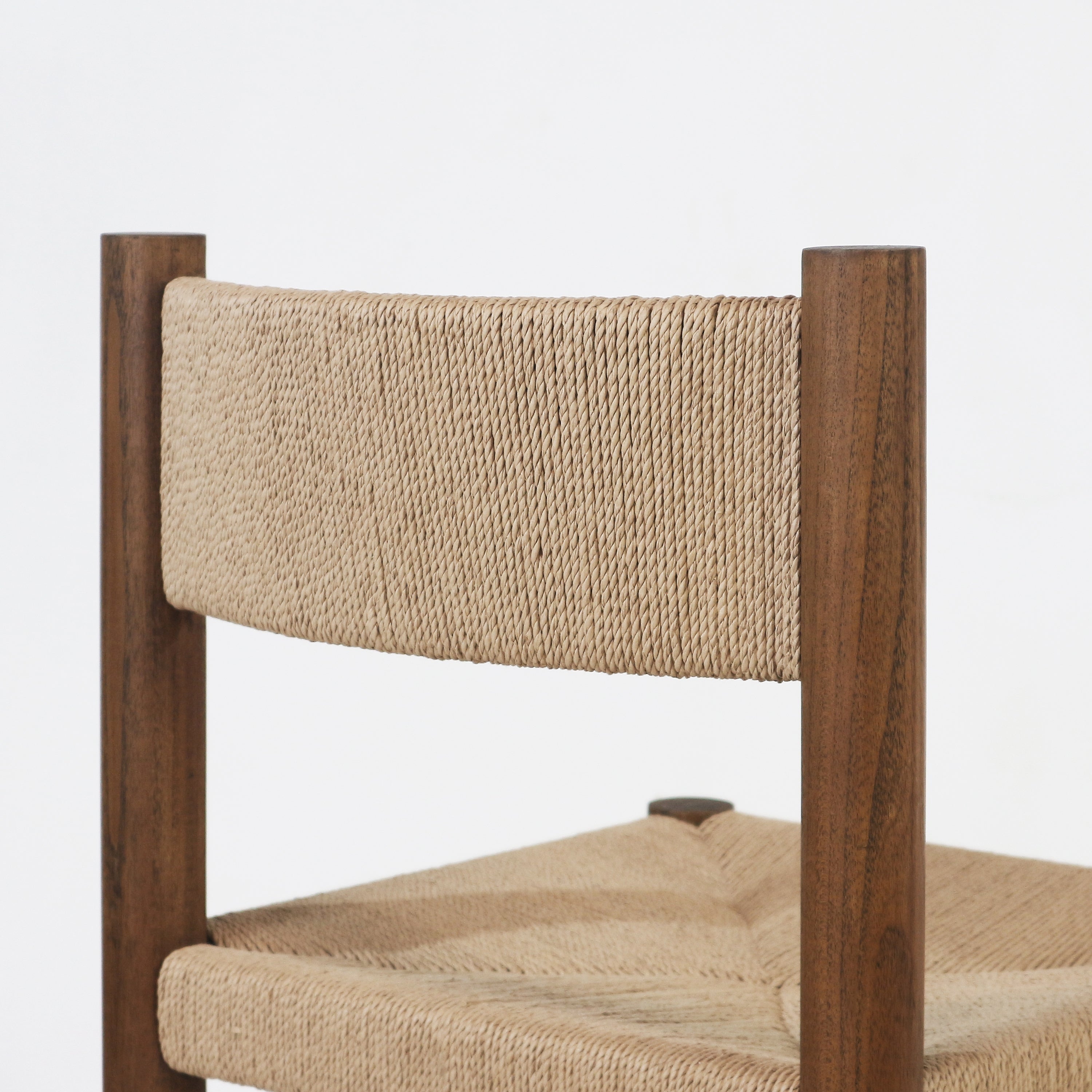 Close-up of a kitchen stool showing a natural papercord woven back and seat with tight rope texture and a warm walnut wood frame featuring rounded vertical posts.