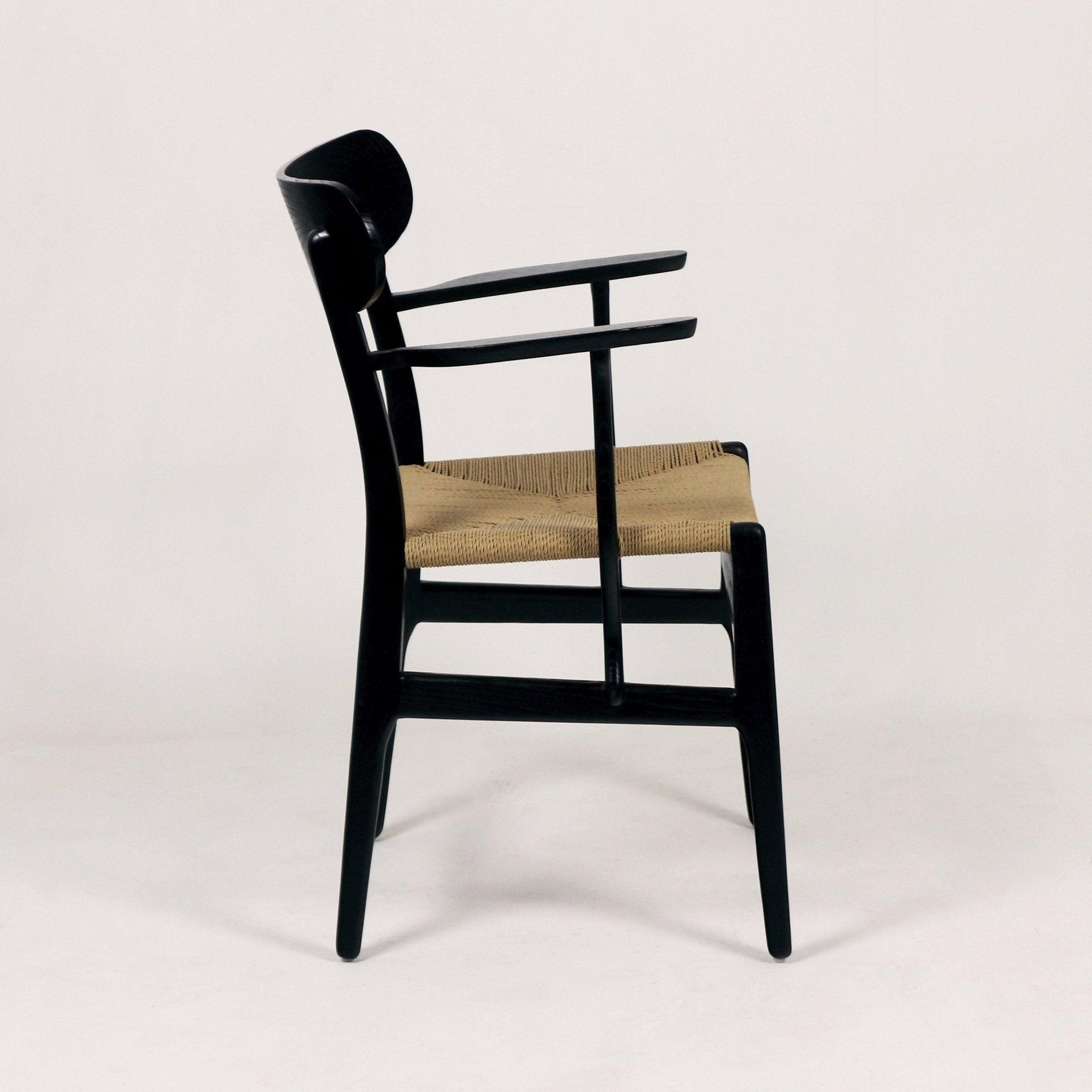 Side view of a modern black solid wood dining chair with curved back and arms and a woven natural rope seat on a neutral background.