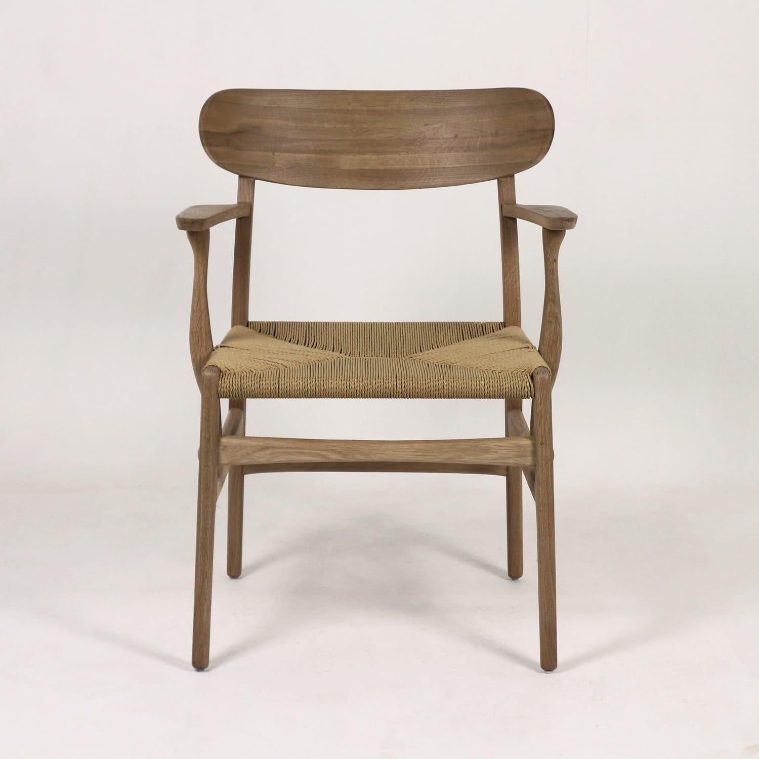 Front view of a Scandi-style solid wood dining chair with a curved wooden backrest, sculpted armrests and a woven natural rope seat in light brown on a neutral white background.