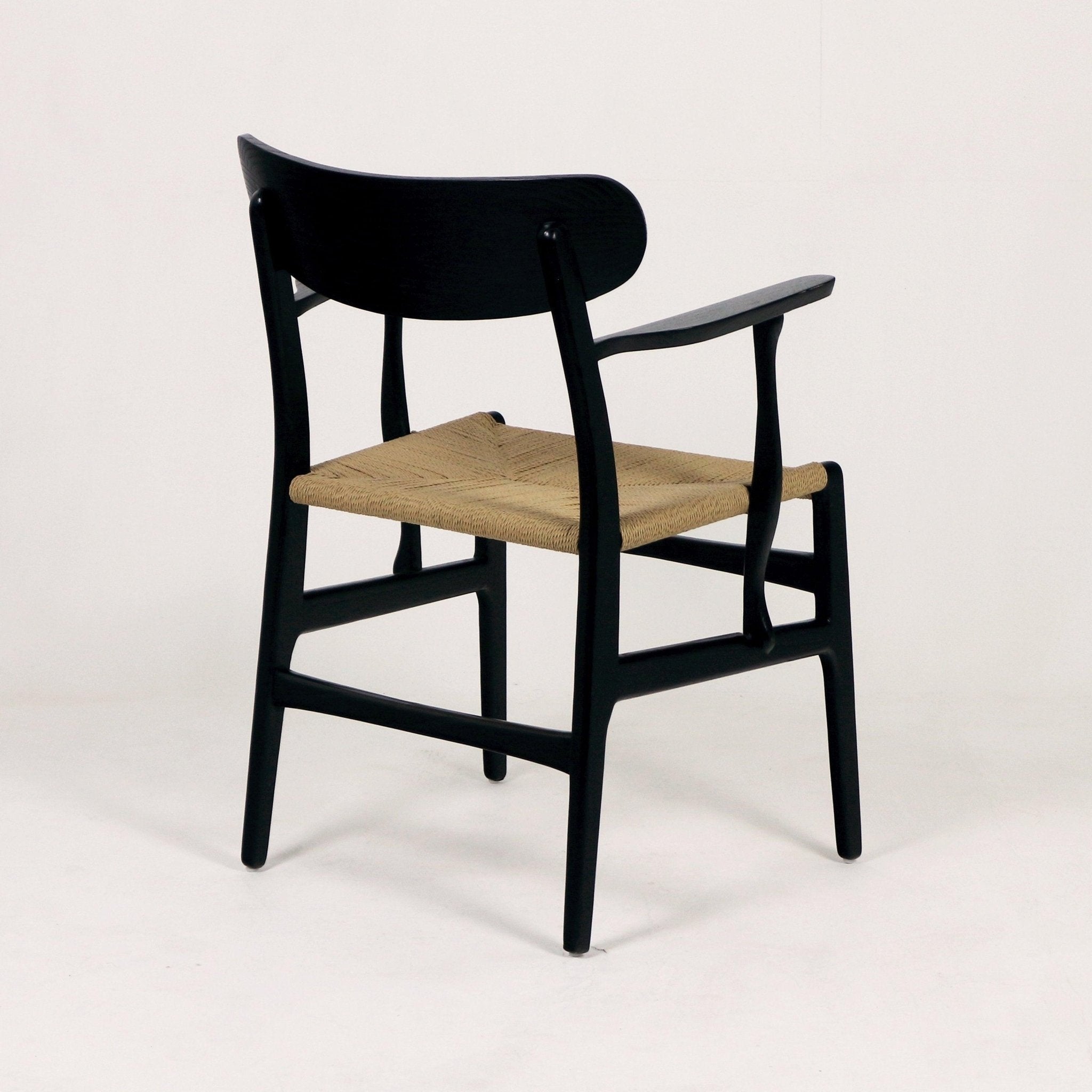 Modern black solid wood dining chair with curved back, slender armrests and woven natural rope seat, shown three-quarter rear view on a white studio background.