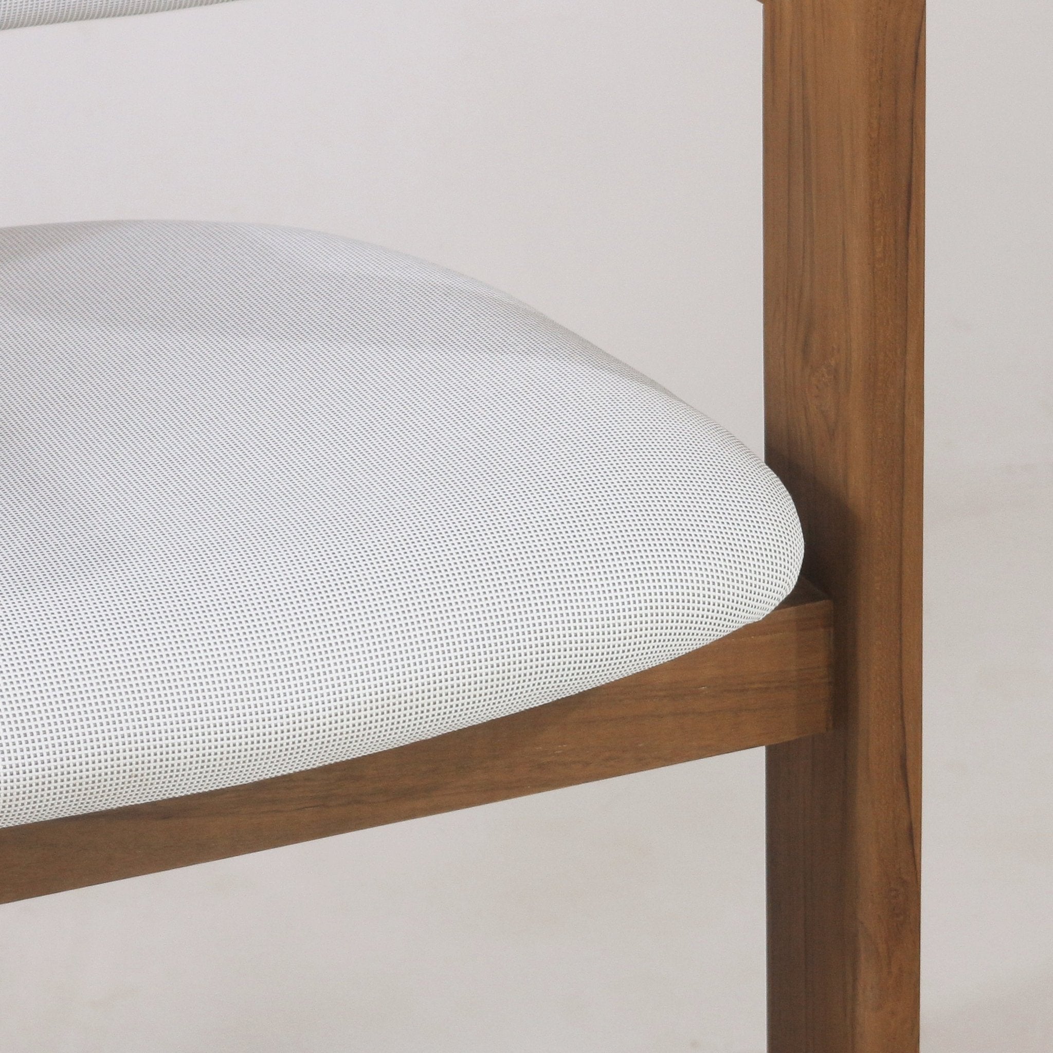 Close-up of a teak outdoor bar stool showing a white textured fabric seat cushion nestled in a curved teak wood frame with a visible straight teak leg.