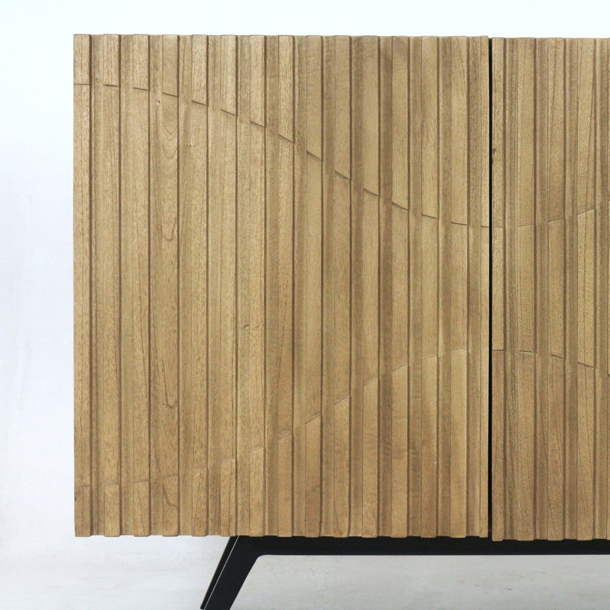 Close-up of a natural teak sideboard showing vertical ribbed front panels with a carved curved pattern and slender black metal legs in a mid-century modern contemporary style.
