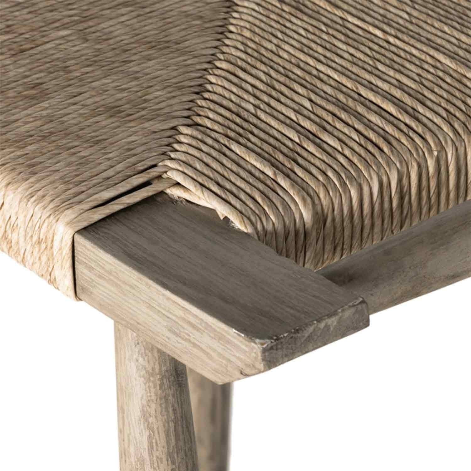 Close-up of a natural teak bar stool seat corner showing tightly woven natural-fiber cord wrapped over a light teak wood frame and rounded teak leg.