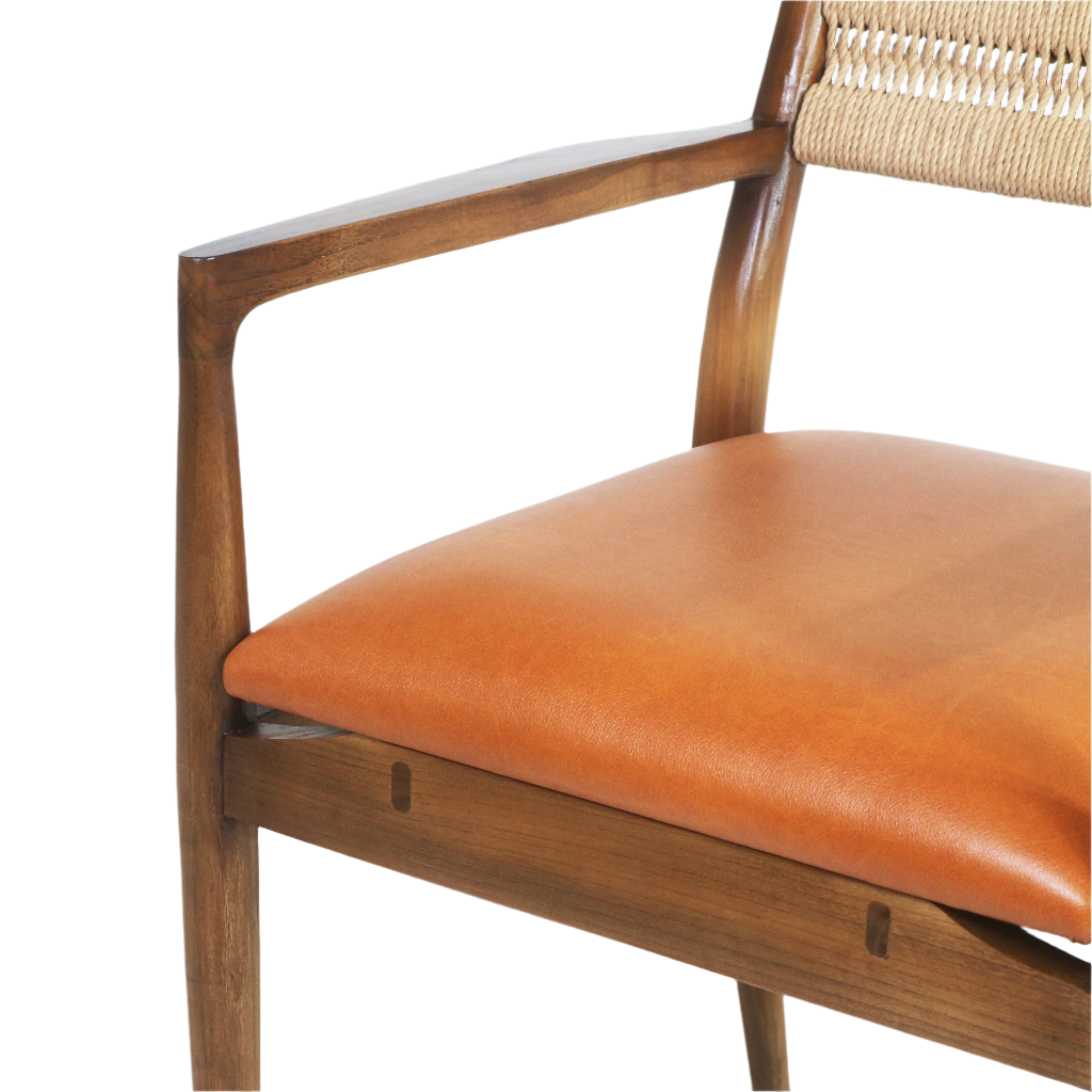 Close-up of a cognac faux-leather dining seat on a natural wood frame with a carved arm and woven rope back visible, highlighting the smooth cushion and tapered wooden joinery.
