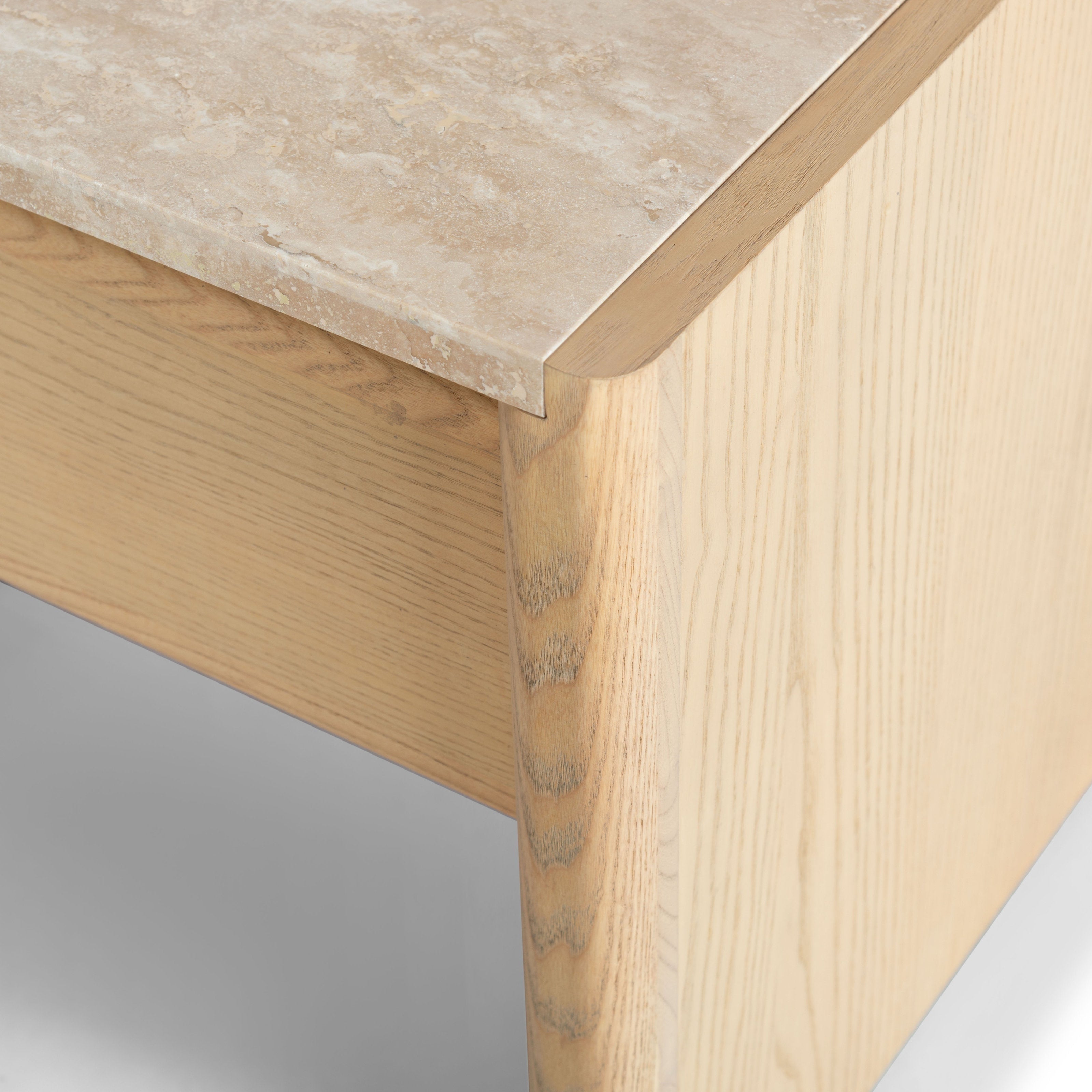 Close-up of a nightstand corner showing a beige marble top and natural light wood grain with a rounded edge and drawer front in a minimalist modern style.