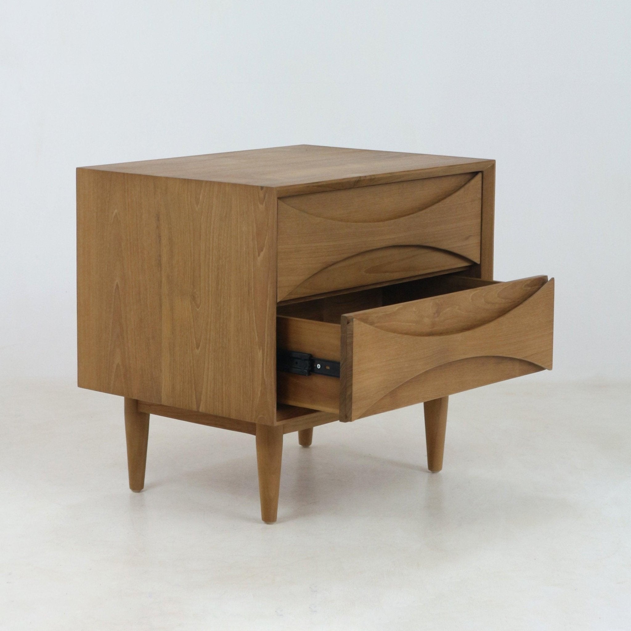 Solid teak nightstand in mid-century Scandinavian style with two drawers, carved recessed pull fronts and tapered legs, photographed on a white background with the lower drawer partially open.