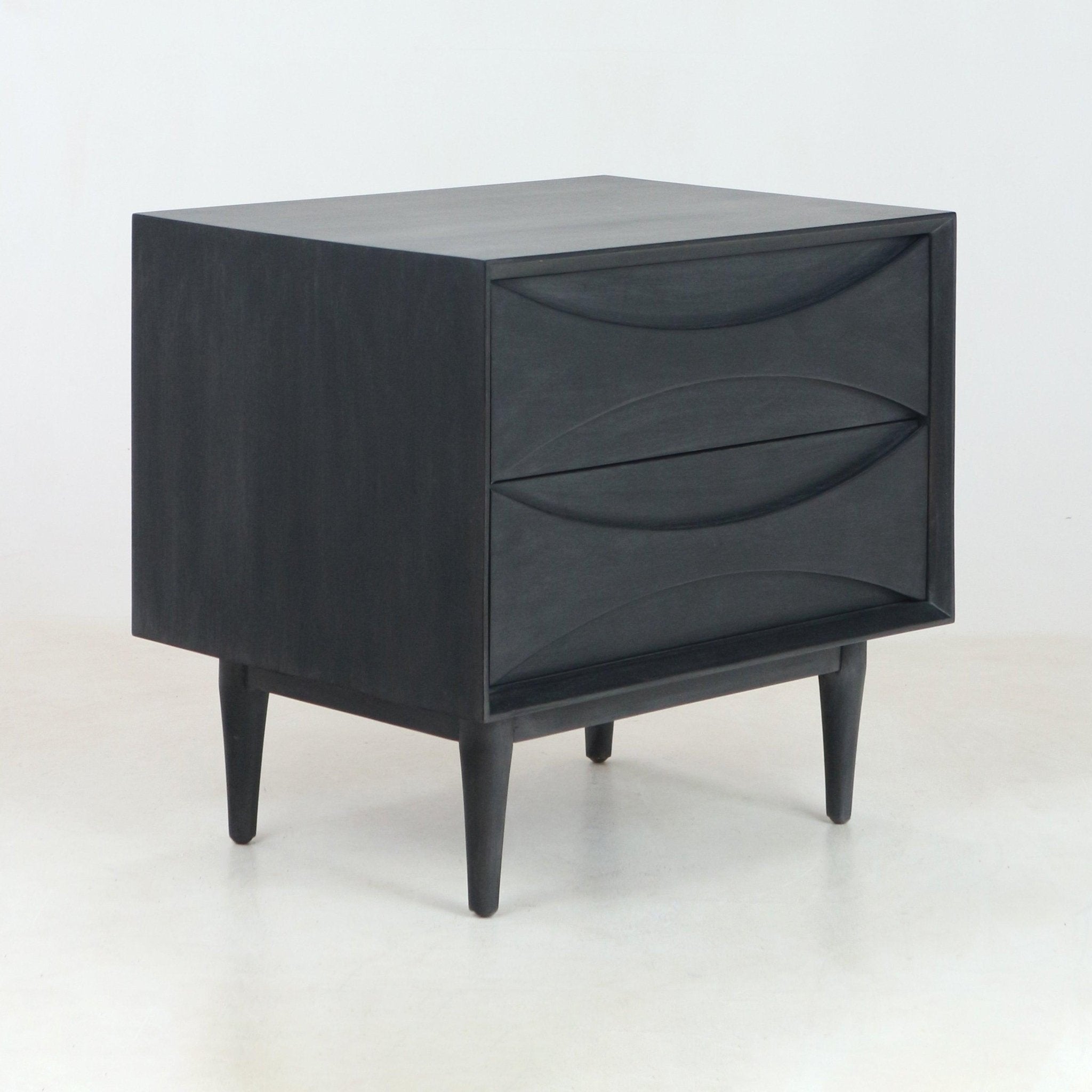 Smoked-black solid wood two-drawer nightstand with sculpted curved drawer fronts and tapered mid-century legs, shown on a light studio floor.