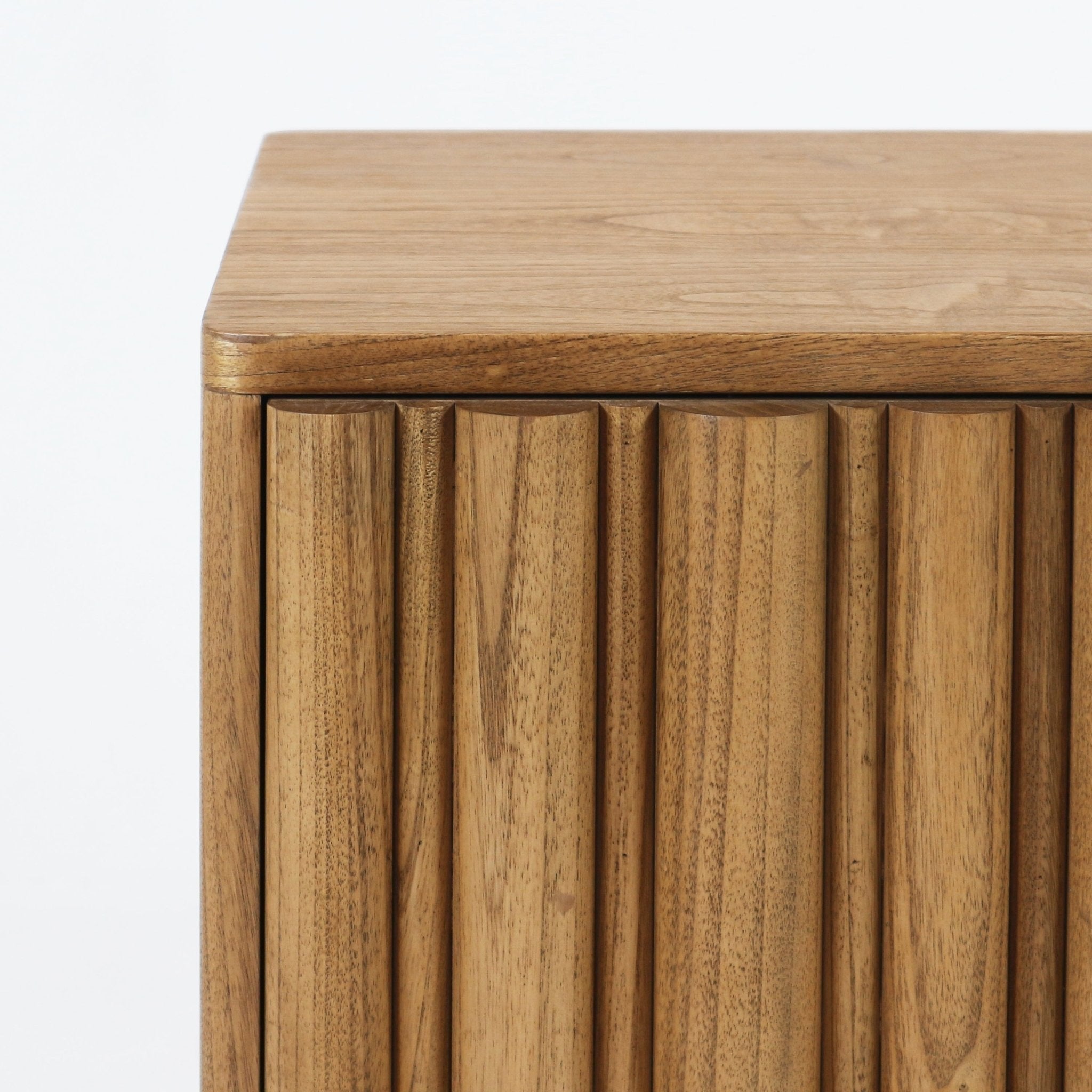 Close-up of a blonde solid wood nightstand corner showing the smooth top and vertical rounded slat drawer front with warm wood grain in a modern Scandinavian style.
