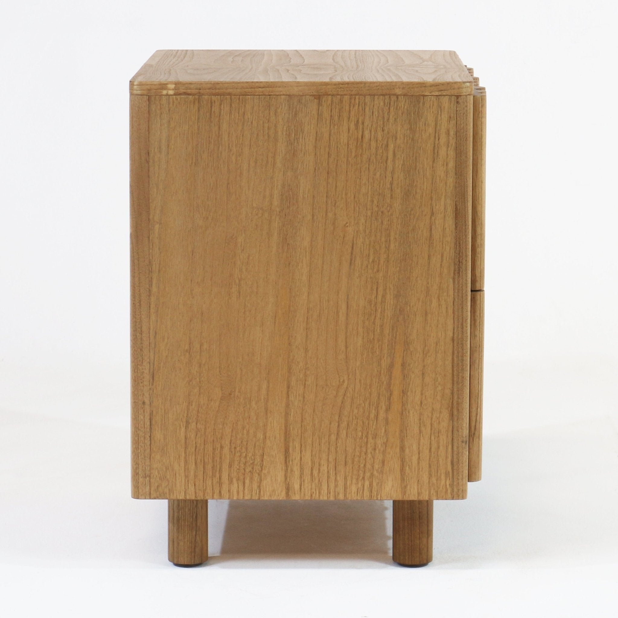 Side view of a Scandinavian-style solid wood nightstand in a blonde natural oak finish showing vertical wood grain, round wooden legs and recessed drawer fronts.