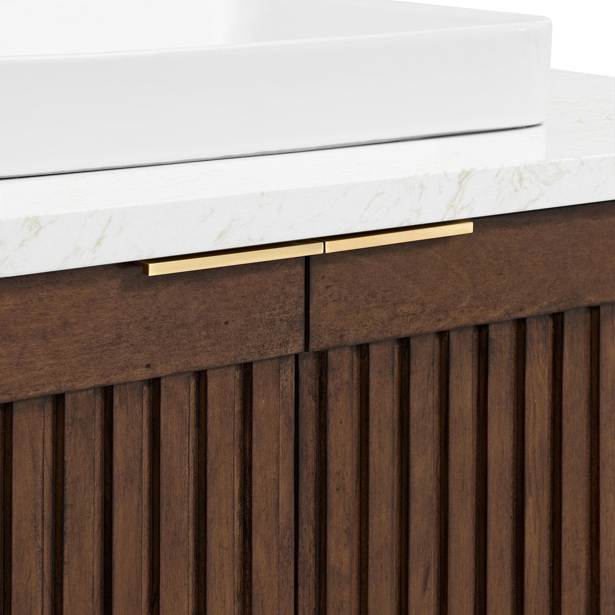 Close-up of a stone countertop with a white ceramic vessel sink sitting above a fluted natural wood vanity in warm brown, accented by slim brass-gold drawer pulls.