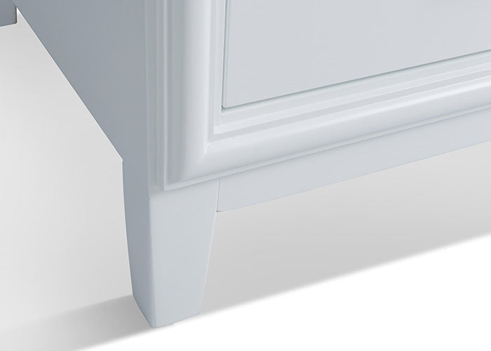 Close-up of the lower corner and tapered leg of a solid wood bathroom vanity in stone finish, showing beveled panel detailing and the base molding.