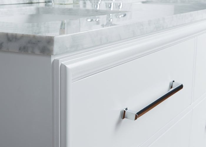 Close-up of a modern white solid-wood bathroom vanity drawer featuring a chrome bar pull and the light stone marble-look countertop edge with part of the double-sink surface and faucet reflection.