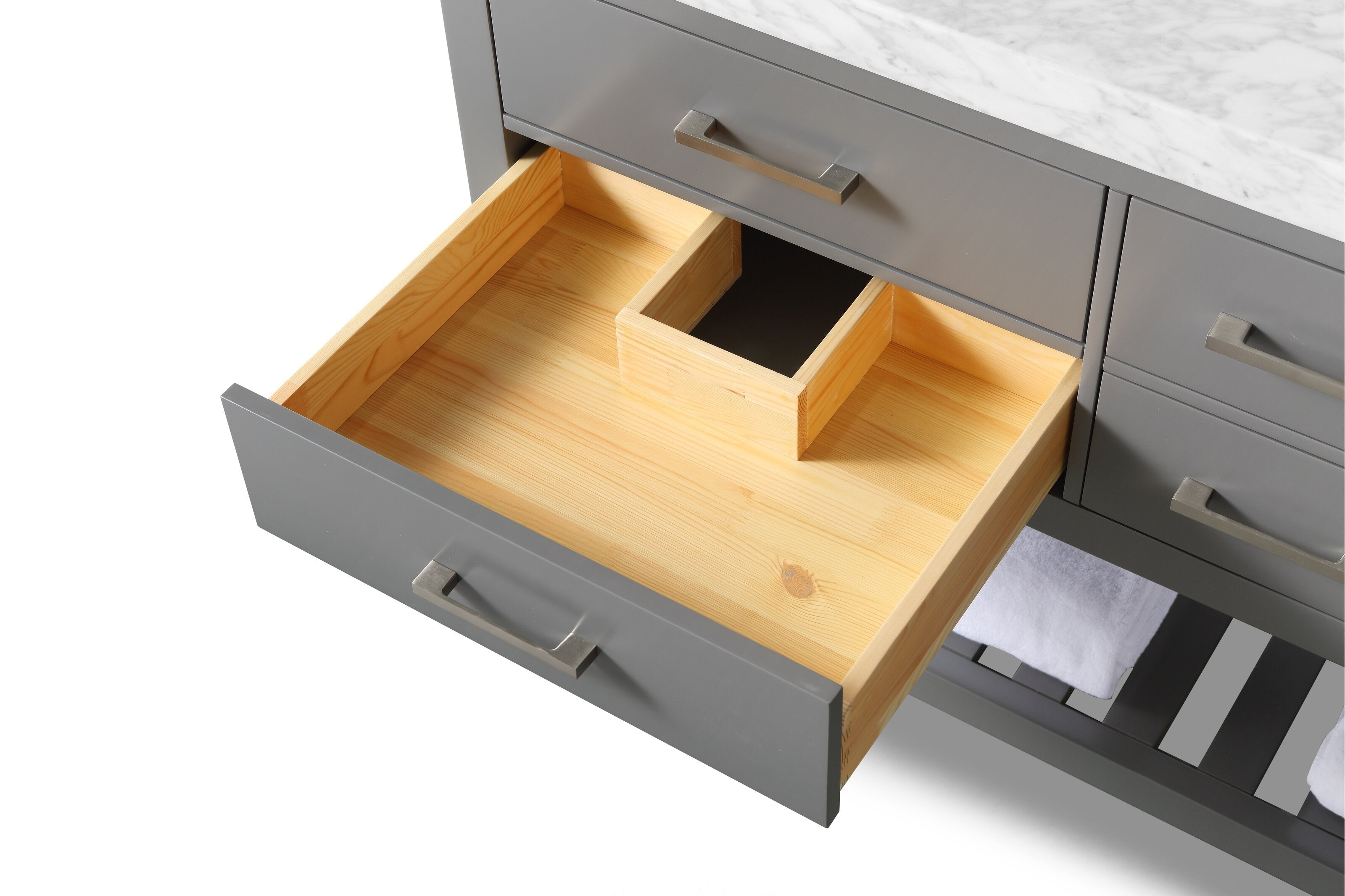 Top-down view of a contemporary stone-colored vanity with a marble top showing an open solid wood drawer with a U-shaped plumbing cutout, gray painted drawer front, brushed metal handles and a slatted lower shelf with towel.