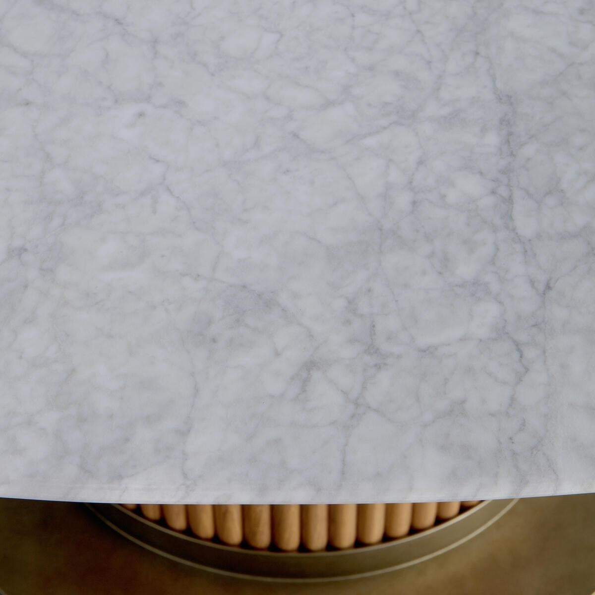 Top-down close-up of a white marble dining tabletop with subtle gray veining over a round oak slatted base and warm brass-finish metal rim.