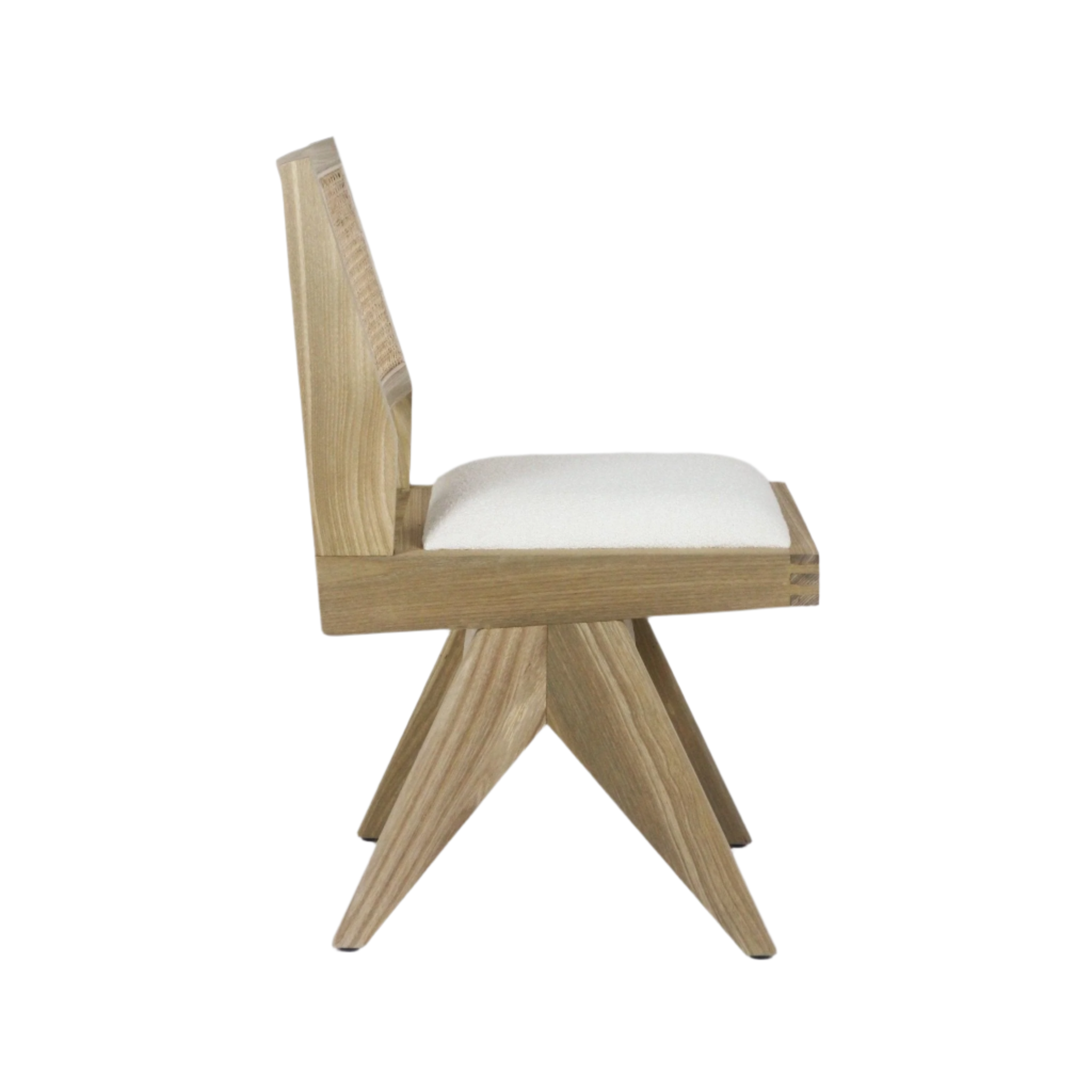 Side profile of an armless dining chair with a natural blonde solid wood frame, angled star-shaped legs, a cream upholstered seat cushion and a low woven cane back.