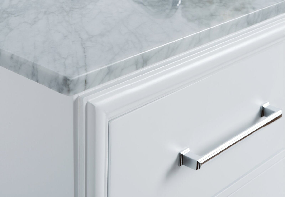 Close-up of a stone countertop on a modern white solid-wood vanity drawer, showing beveled molding and a polished chrome bar handle highlighting the marble-look top and hardware detail.