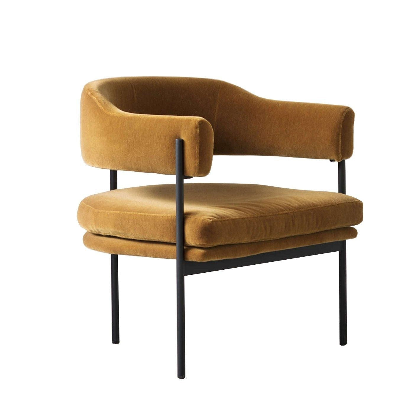Mustard velvet lounge chair with a curved low back, open-sided armrests, plush double-layer seat cushion and slim black metal legs and supports, shown on a white background.