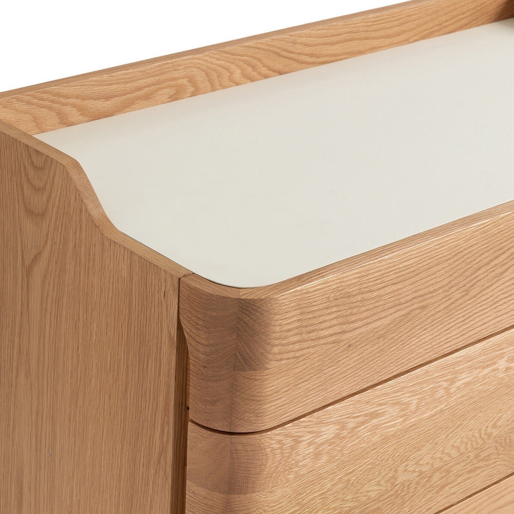 Close-up of a blonde solid wood dresser corner showing rounded drawer fronts, visible natural wood grain and a smooth white linoleum top with a shallow raised back lip.