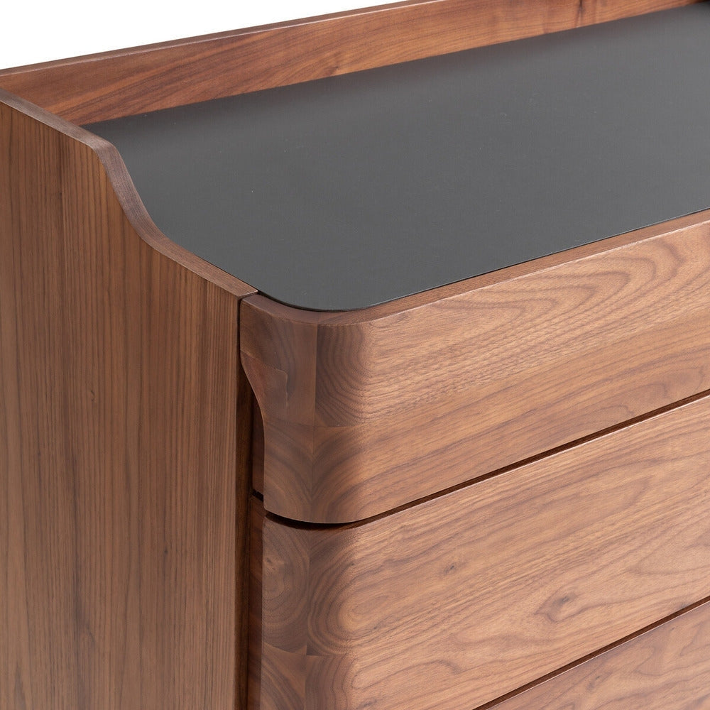Close-up of a solid walnut armoire dresser corner showing smooth, rounded drawer fronts and a black linoleum inset top, highlighting walnut grain and seamless modern joinery.